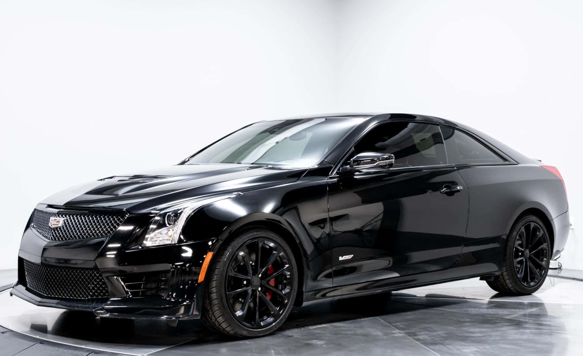 Cadillac Ats 桌布 壁紙 — 一輛亮黑色Cadillac ATS-V雙門轎跑車，配備紅色制動卡鉗和黑色輪圈，在反射的攝影棚地板上，以純白背景為襯，蓄勢待發。