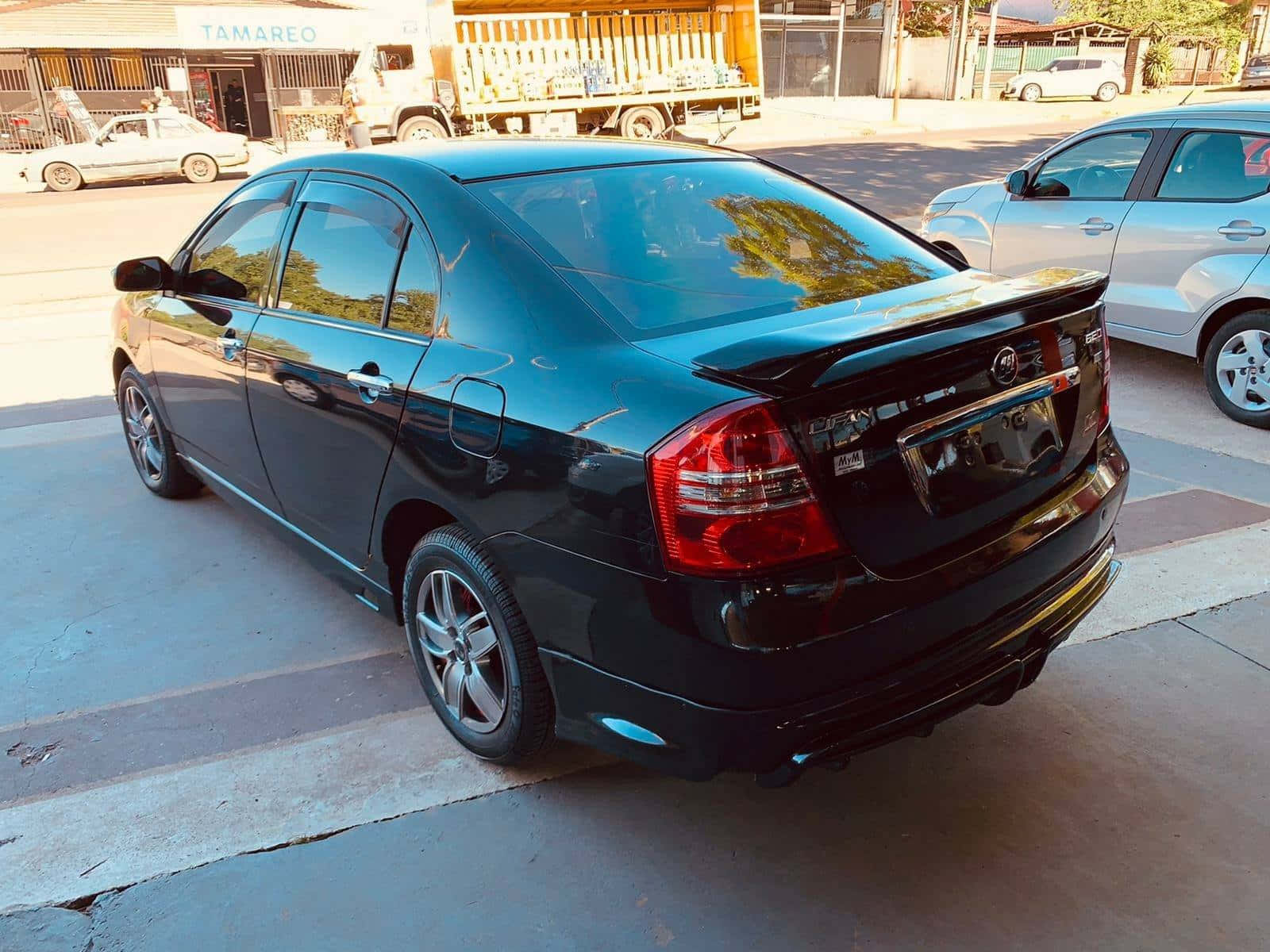  壁紙 — 一輛亮黑色轎車停放在陽光明媚的城市街道上，背景有其他車輛和商店門面。