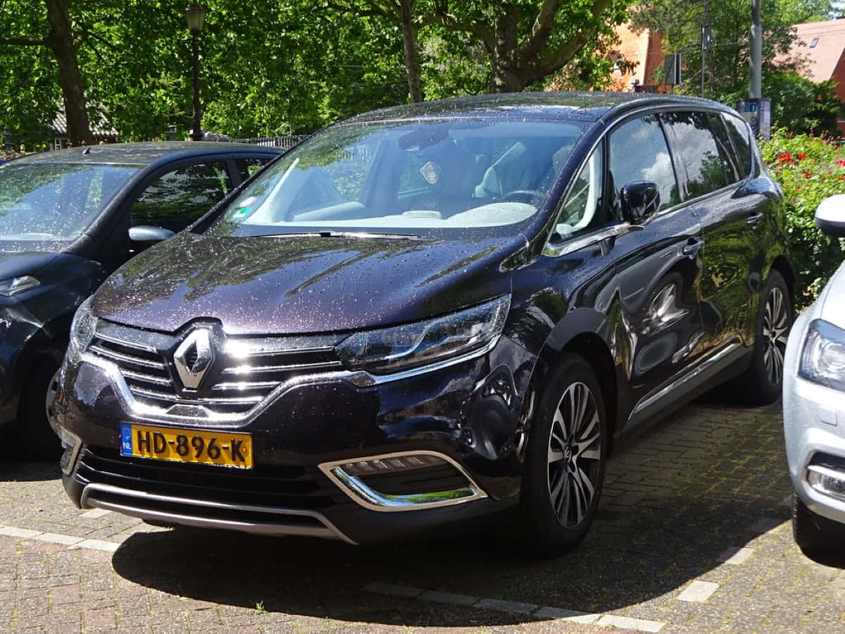 Renault Espace 桌布 壁紙 — 一輛亮黑色雷諾Espace停放在陽光普照的磚地停車場，附近有樹木和其他車輛。