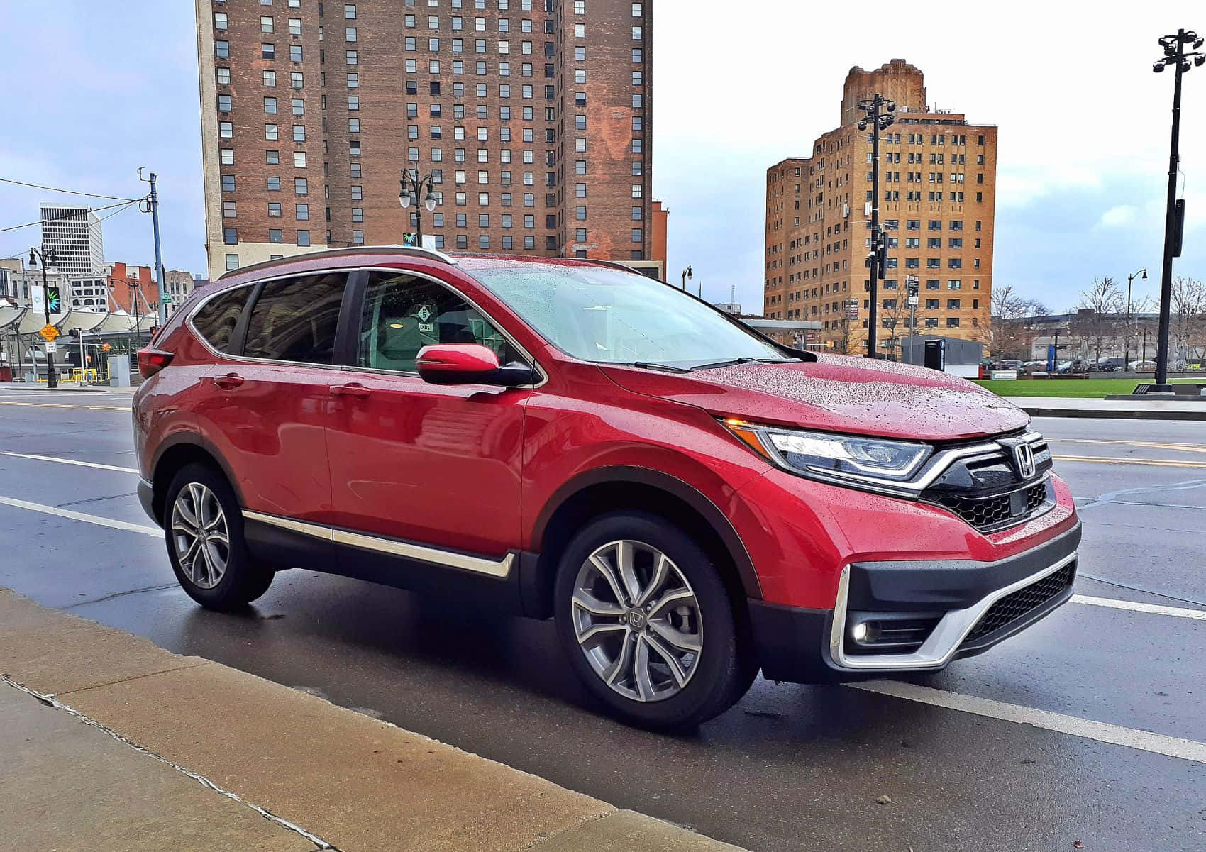 Honda Cr-v 桌布 壁紙 — 一輛亮紅色本田CRV SUV停泊在潮濕的城市街道上，背景是磚砌建築，天空多雲。