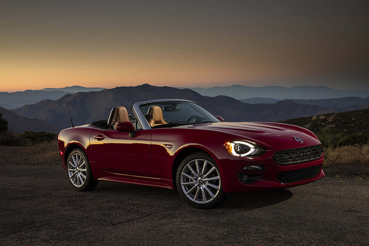 Fiat 124 Spider 桌布 壁紙 — 一輛亮紅色敞篷跑車停泊在日落時分的山路上，背景是層層疊疊的山脈。