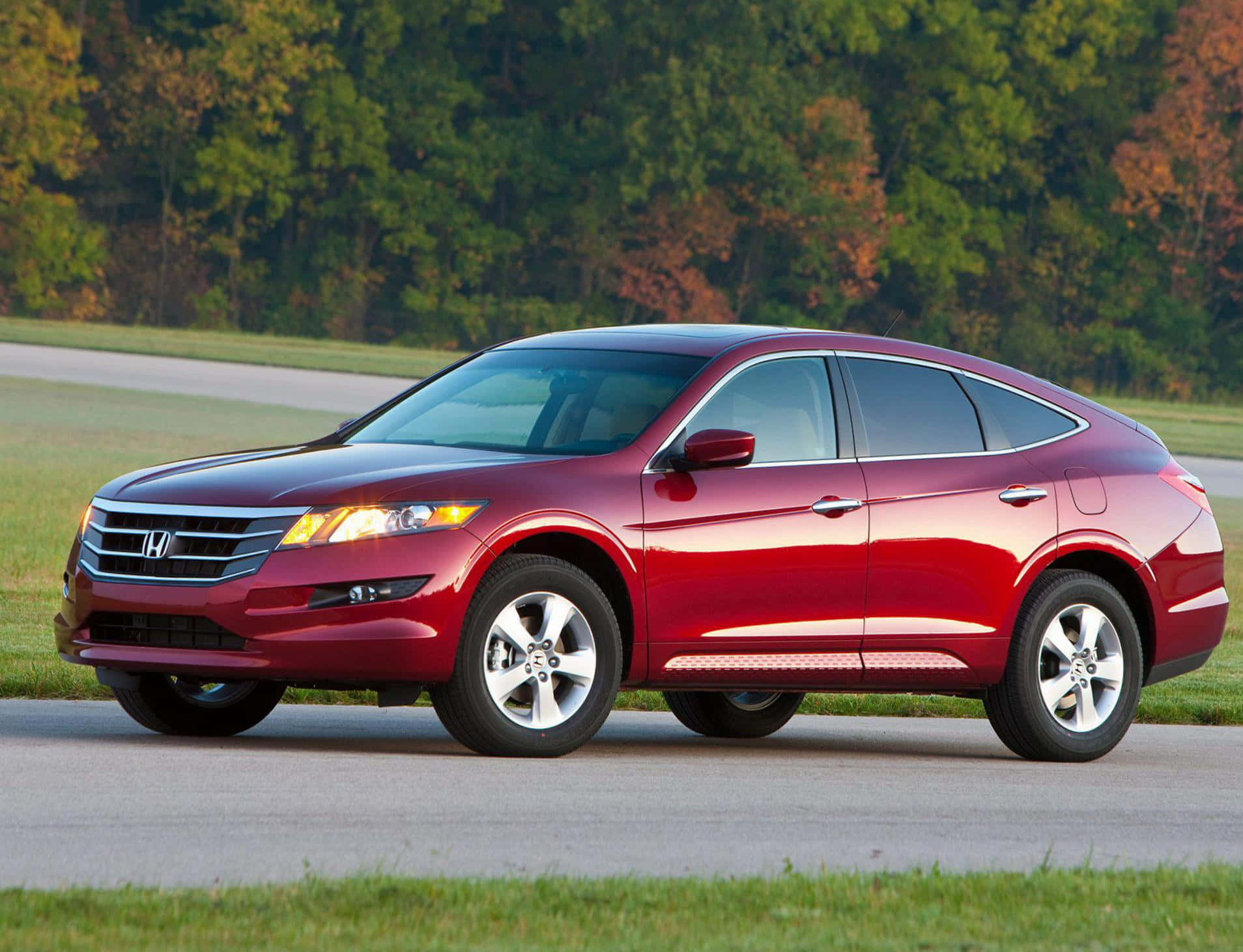 Honda Crosstour 桌布 壁紙 — 一輛亮紅色的本田 Crosstour SUV 沿著一條鋪砌的道路行駛，道路兩旁是秋天的樹木和草地。
