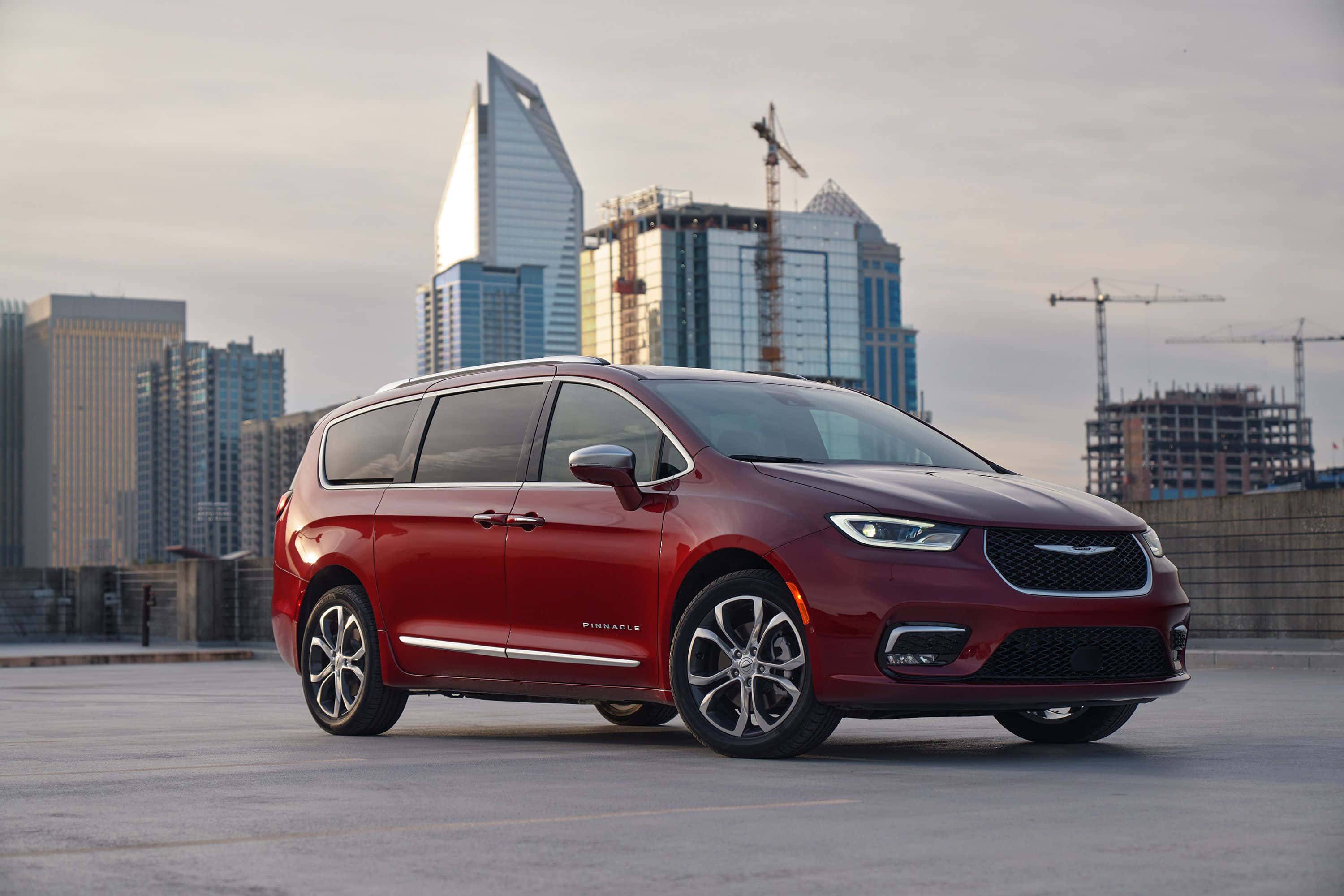 Chrysler Pacifica 桌布 壁紙 — 一輛亮紅色的Chrysler Pacifica小型貨車停放在屋頂上，背景是現代城市天際線和建築起重機。