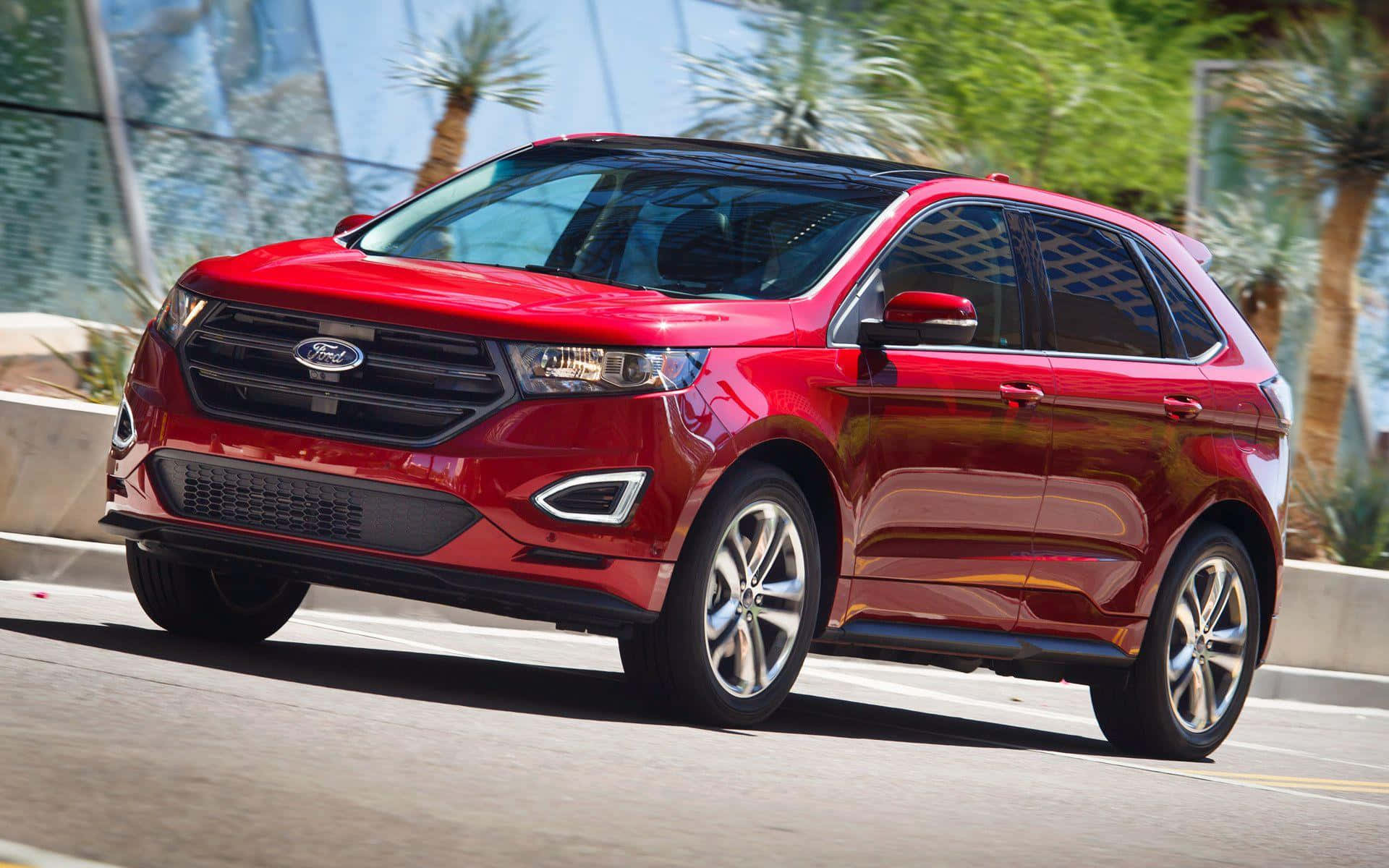Ford Edge 桌布 壁紙 — 一輛亮紅色的福特Edge SUV在陽光明媚的城市街道上行駛，街道兩旁種滿棕櫚樹和玻璃建築。