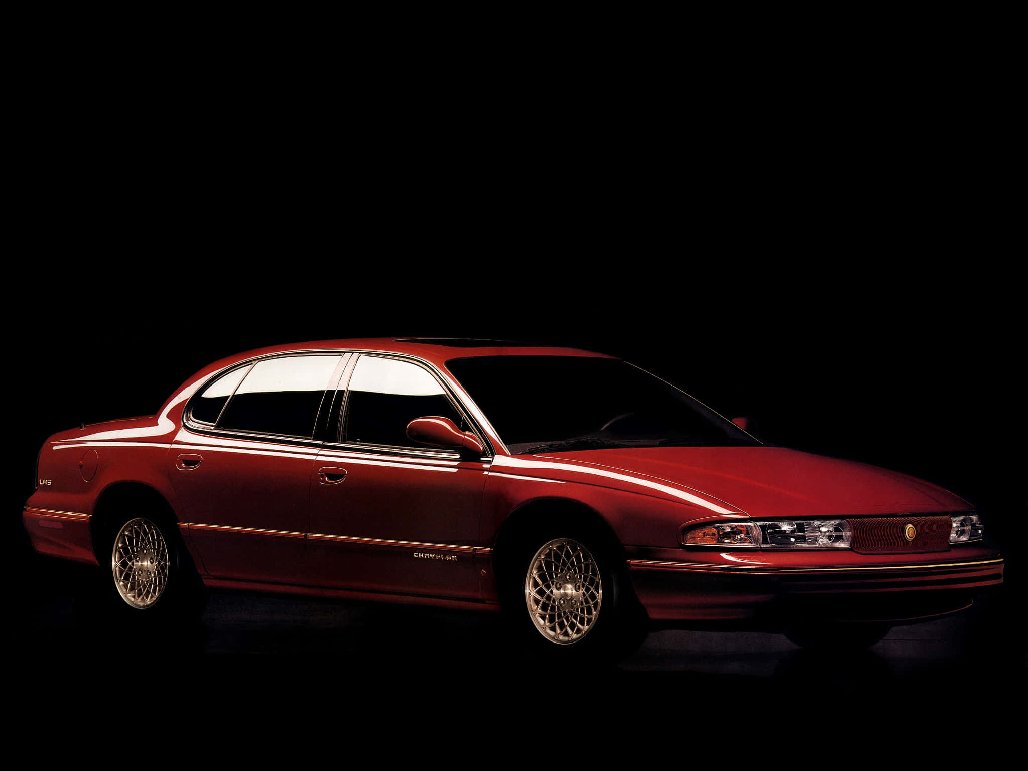 Chrysler Lhs 桌布 壁紙 — 一輛亮紅色的克萊斯勒轎車在純黑背景下的攝影棚燈光中閃耀，展現其流暢線條和鍍鉻輪圈。