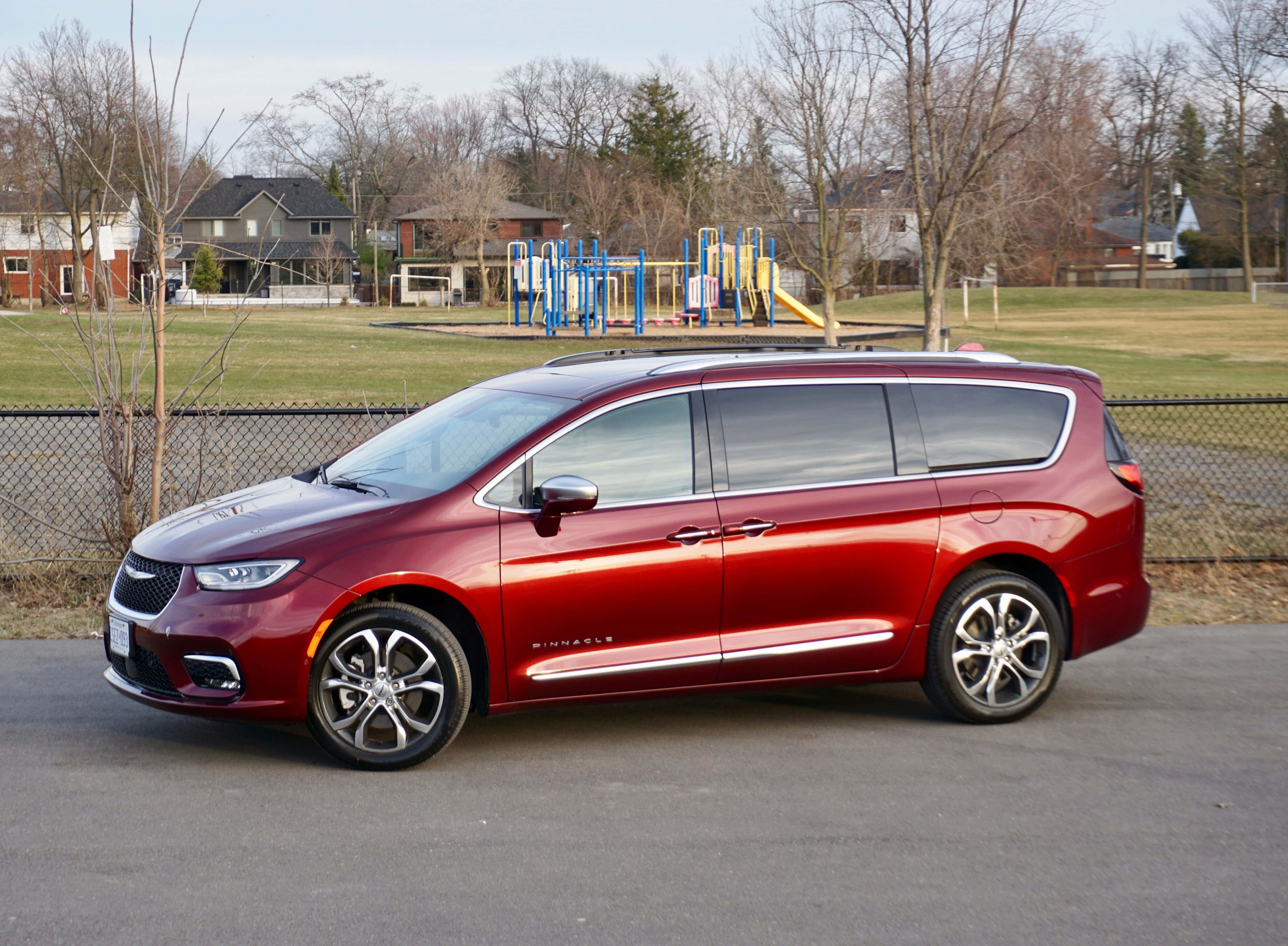 Chrysler Pacifica 桌布 壁紙 — 一輛亮紅色的克萊斯勒 Pacifica 小型貨車停在柏油路上，背景有遊樂場和光禿禿的樹木。