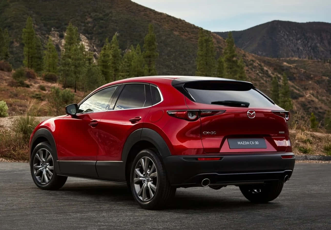 Mazda Cx-30 桌布 壁紙 — 一輛亮紅色的Mazda CX-30 SUV停在瀝青路上，背景是山區地形和散落的松樹。