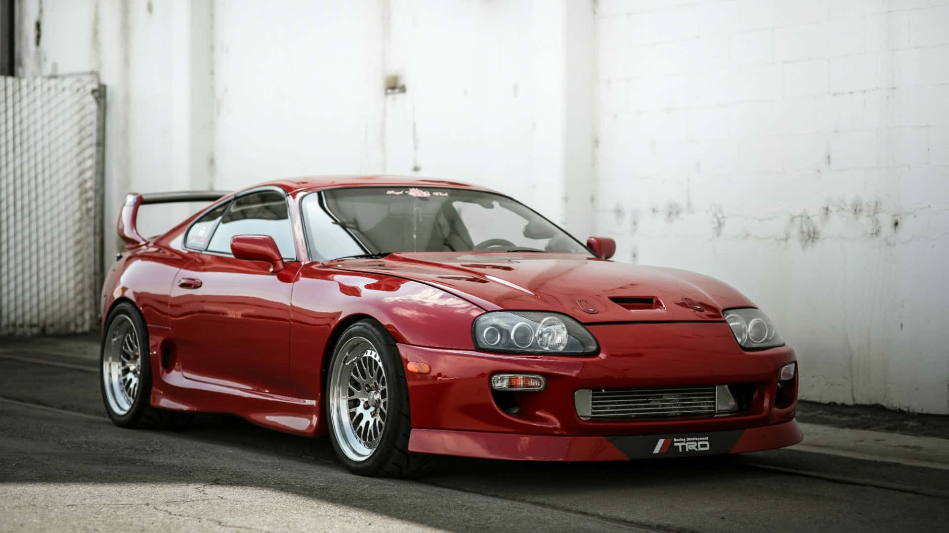 紅色豐田Supra跑車停靠在白色混凝土牆旁。 — Toyota Supra 壁紙