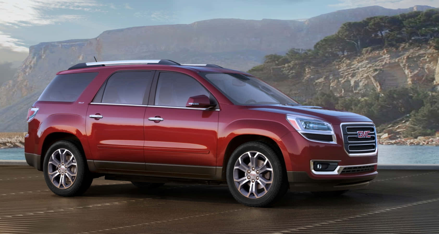 Gmc Acadia 桌布 壁紙 — 一輛亮紅色的GMC Acadia SUV停泊在木製碼頭上，背景是山脈和樹木，天空晴朗。