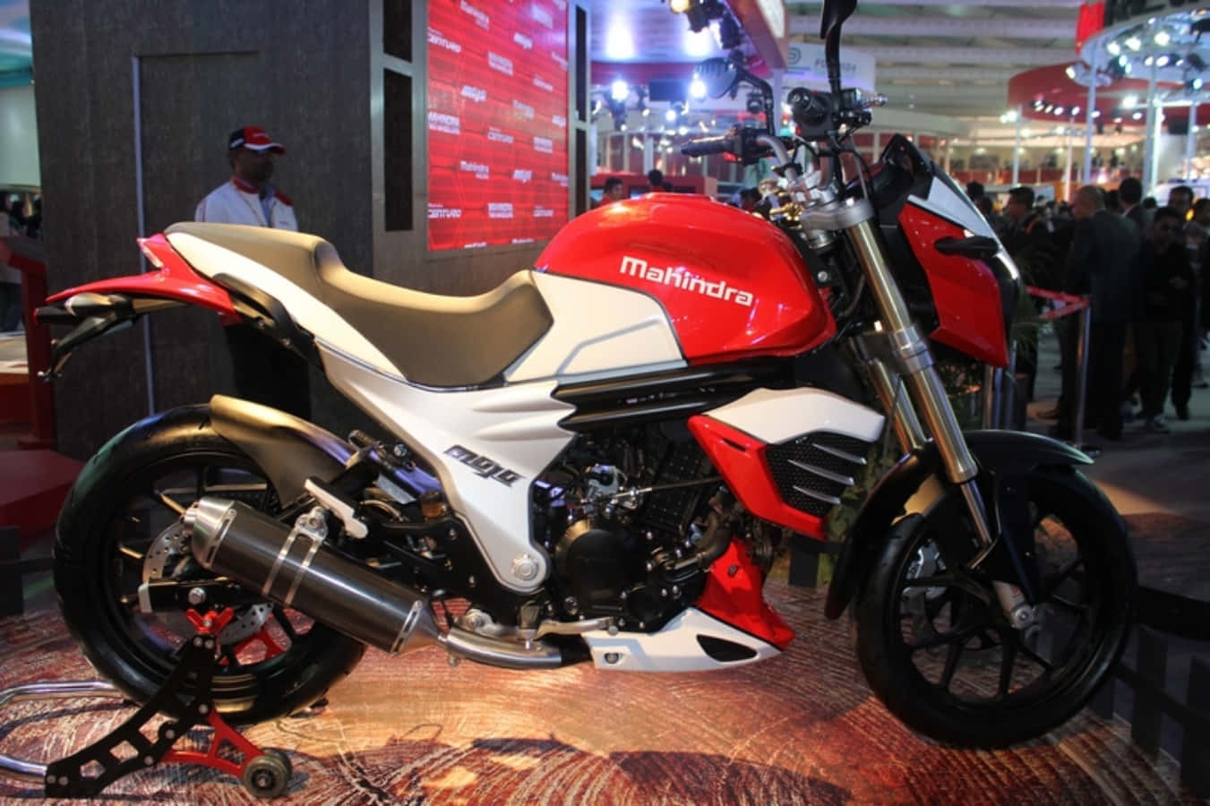 Mahindra Mojo 桌布 壁紙 — 一輛紅色和白色的Mahindra Mojo機車在光線明亮的室內車展中展出，背景有人群。