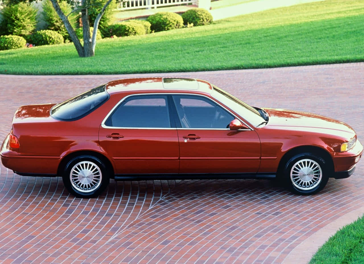 Acura Legend 桌布 壁紙 — 一輛亮紅色轎車停泊在彎曲的磚砌車道上，背景是修剪整齊的綠色草坪和樹木。