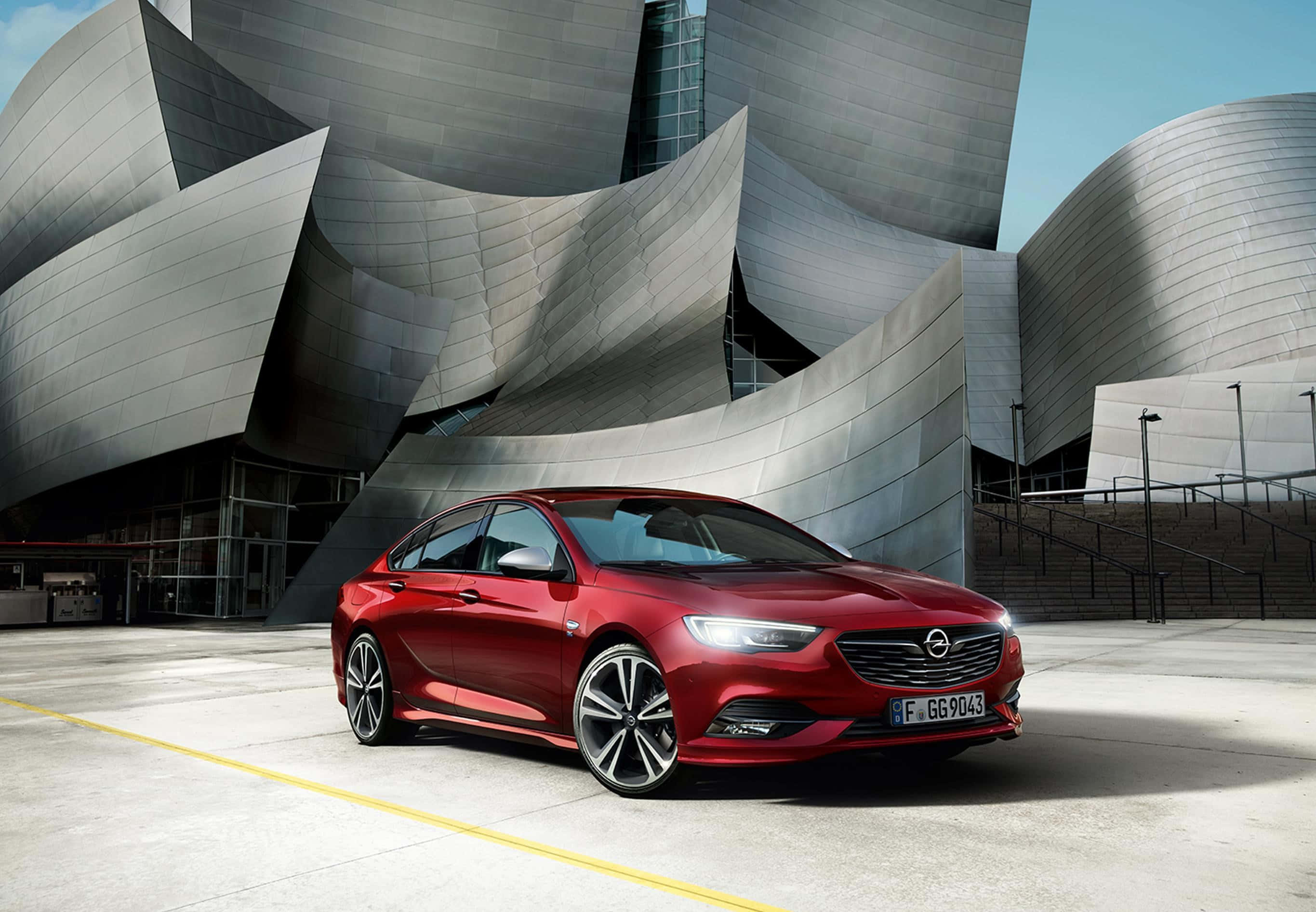 Opel Insignia 桌布 壁紙 — 一輛亮紅色的Opel轎車停在標誌性的鈦金屬外牆Walt Disney Concert Hall前，在明亮的日光下。