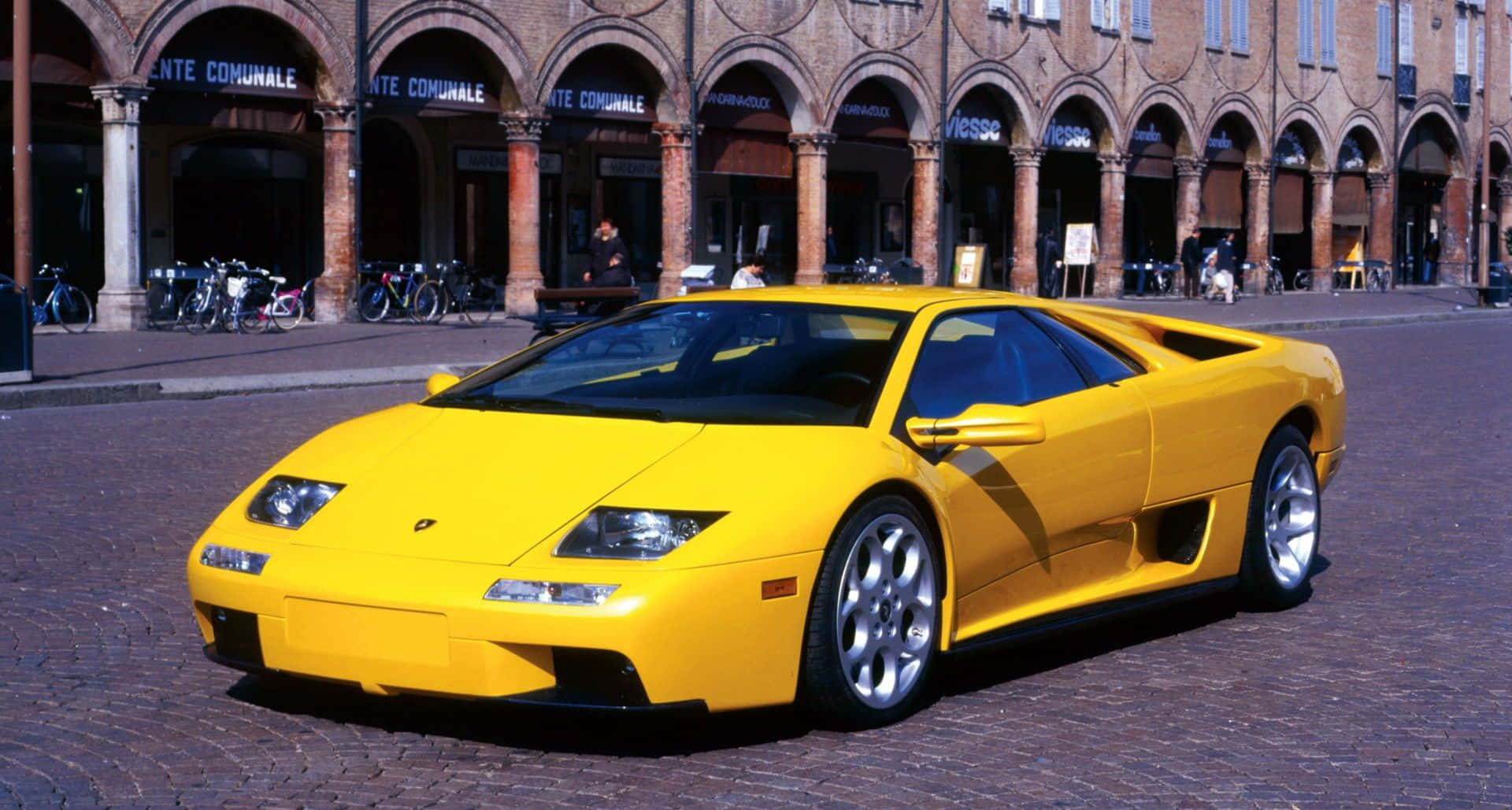Lamborghini Diablo 桌布 壁紙 — 一輛亮黃色的藍寶堅尼Diablo跑車停泊在鵝卵石廣場上，背景是拱形磚建築。