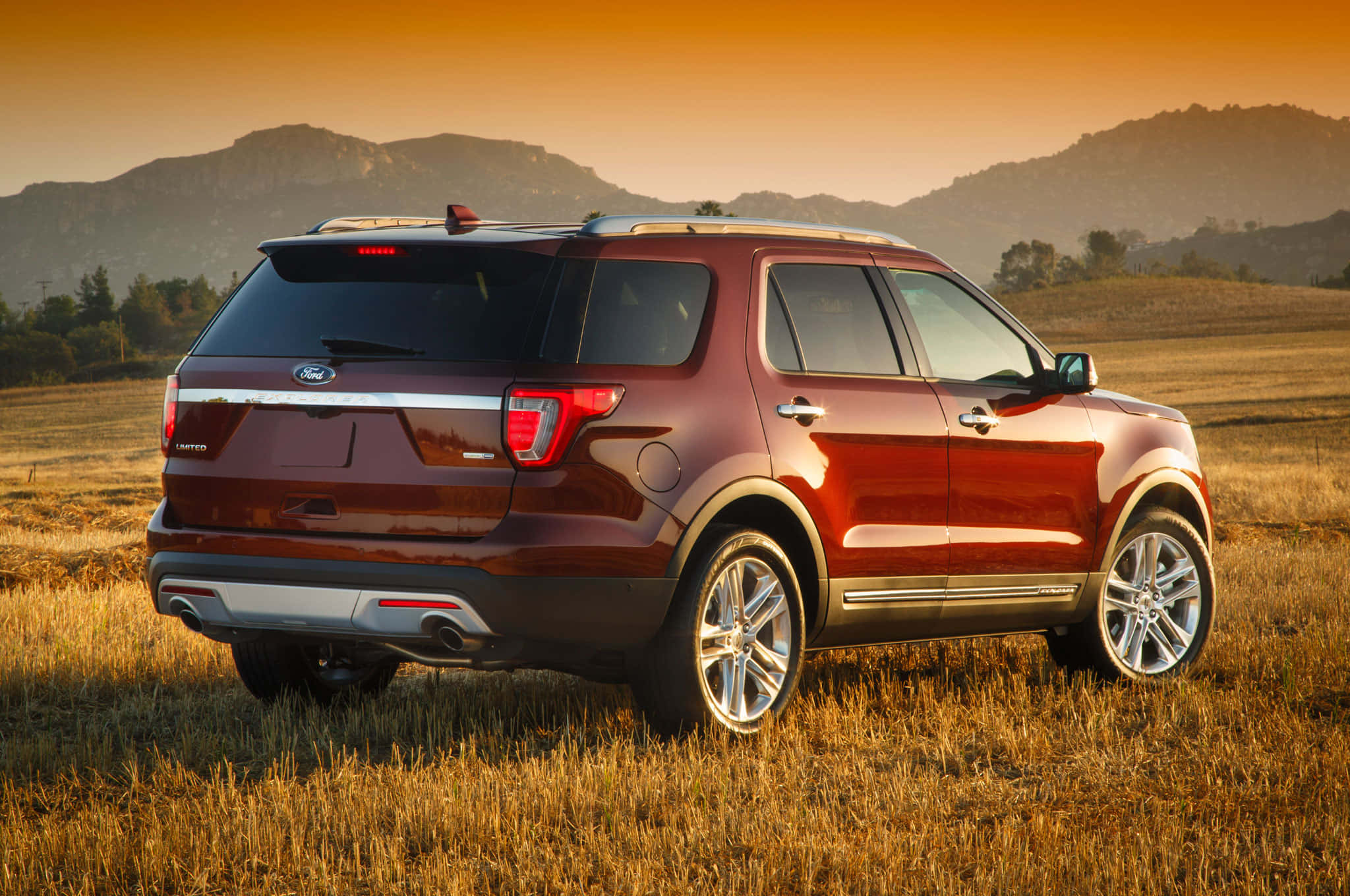 Ford Explorer 桌布 壁紙 — 一輛酒紅色福特探險者SUV停在日落時分的金色田野中，背景有山脈。