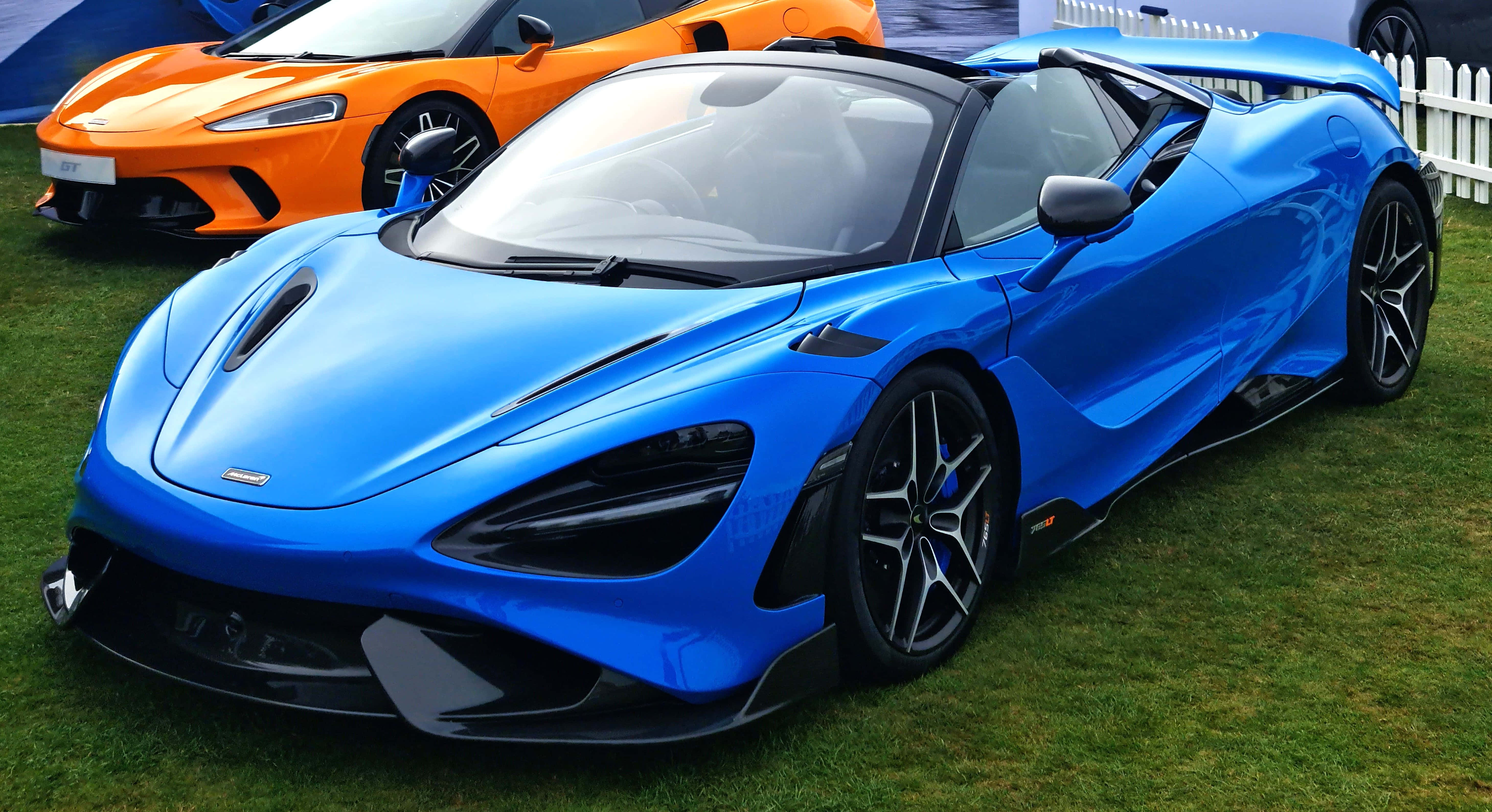 Mclaren 765lt 桌布 壁紙 — 一輛亮藍色McLaren Senna跑車停在草地上，後面有一輛橙色超級跑車。