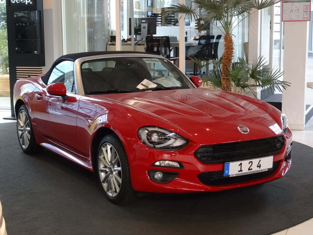 Fiat 124 Spider 桌布 壁紙 — 一輛亮紅色的菲亞特124 Spider敞篷車在棕櫚樹旁的展示間燈光下閃閃發光。