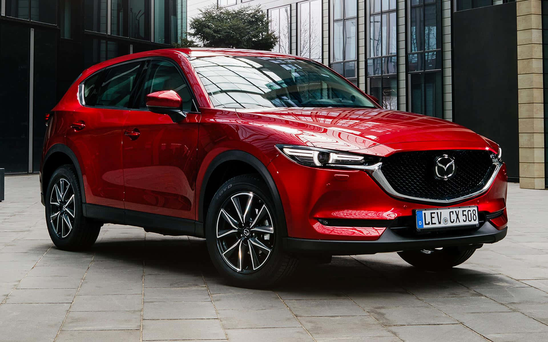 Mazda Cx-5 桌布 壁紙 — 一輛亮紅色Mazda CX-5 SUV停放在現代玻璃建築前的瓷磚廣場上。