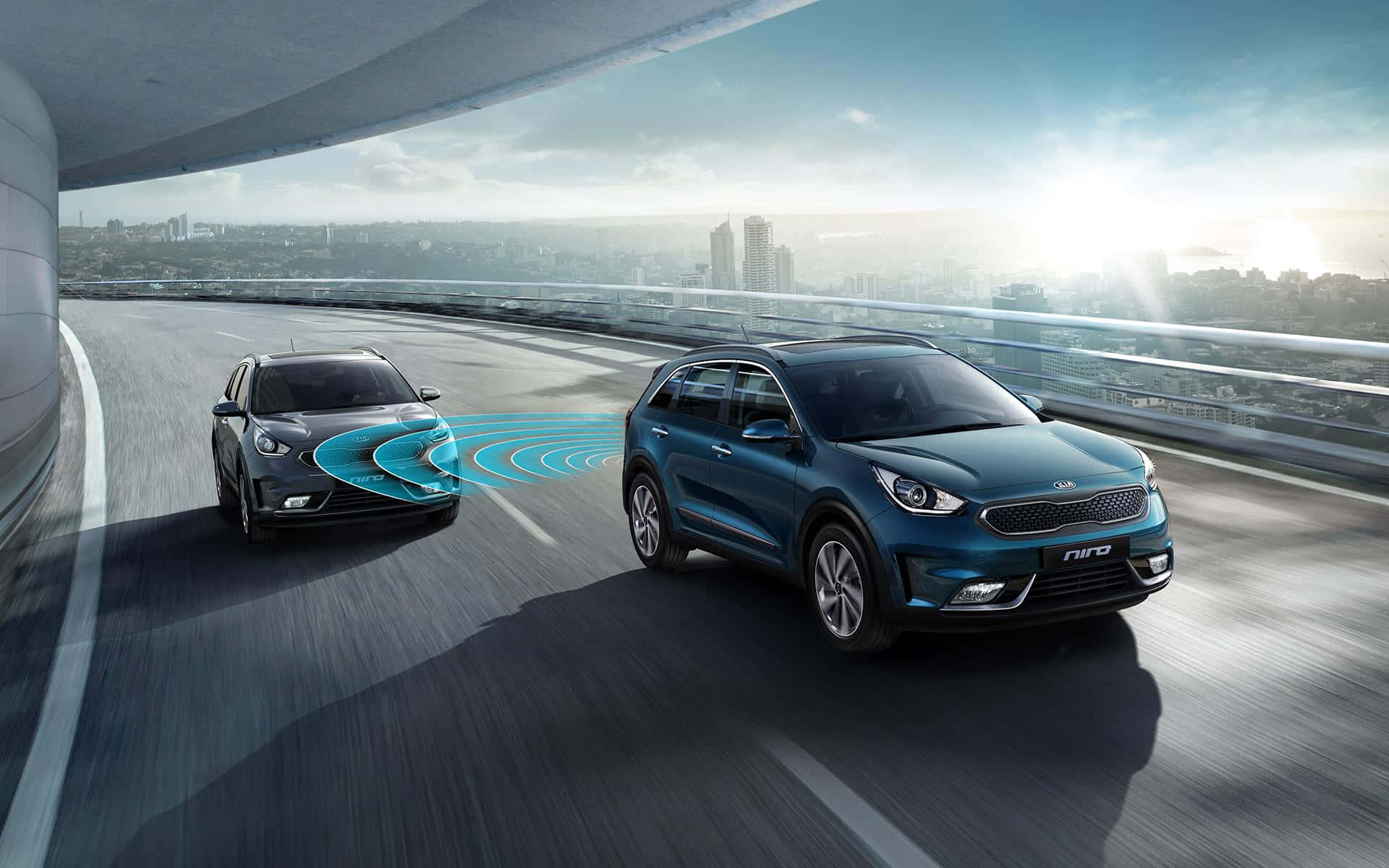 Kia Niro 桌布 壁紙 — 兩輛Kia Niro SUV並排行駛在現代化的高架公路上，背景是城市天際線。