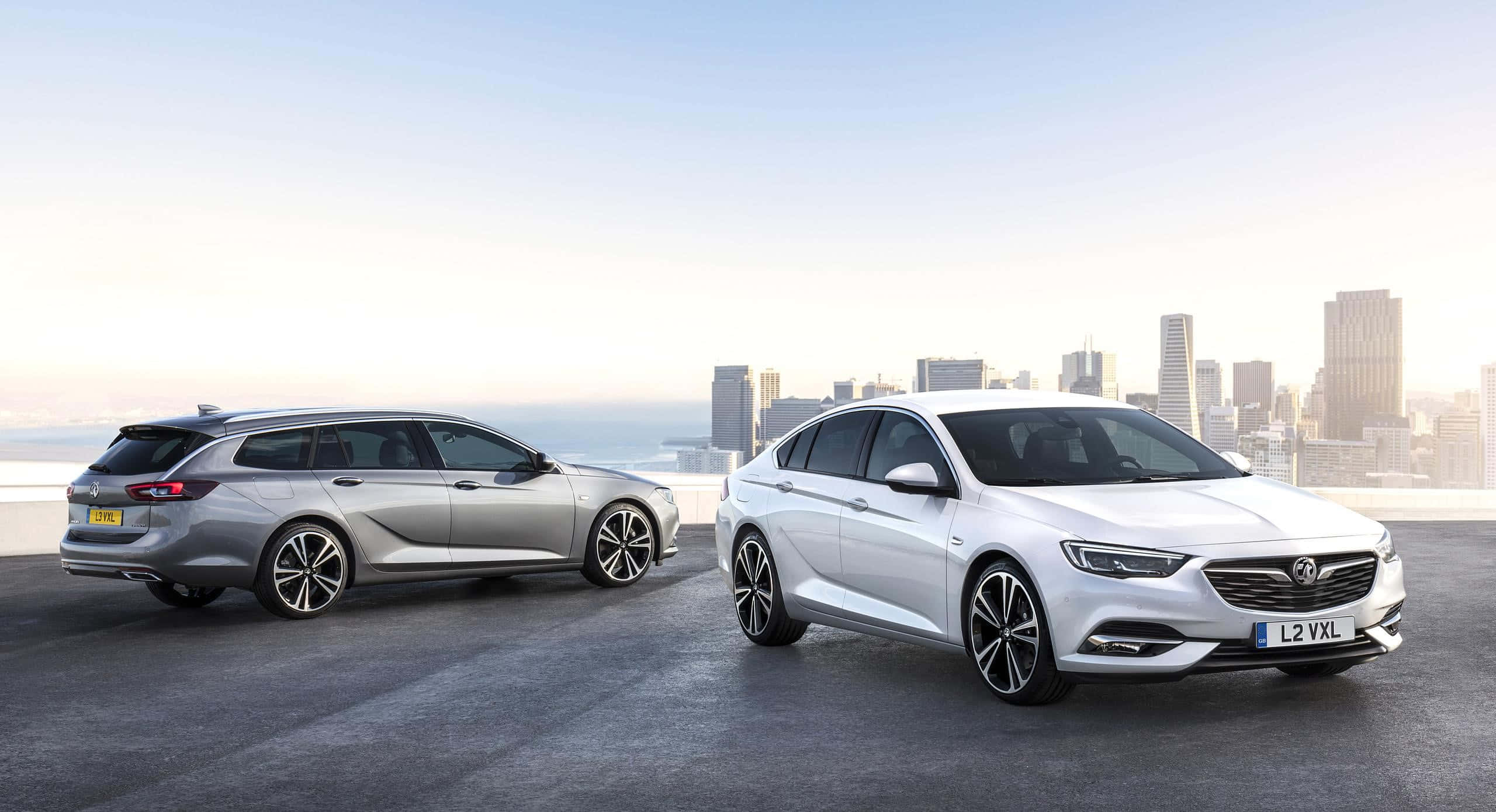 Opel Insignia 桌布 壁紙 — 兩輛時尚現代汽車銀色和白色停泊在屋頂上，俯瞰黃金時段的城市天際線。