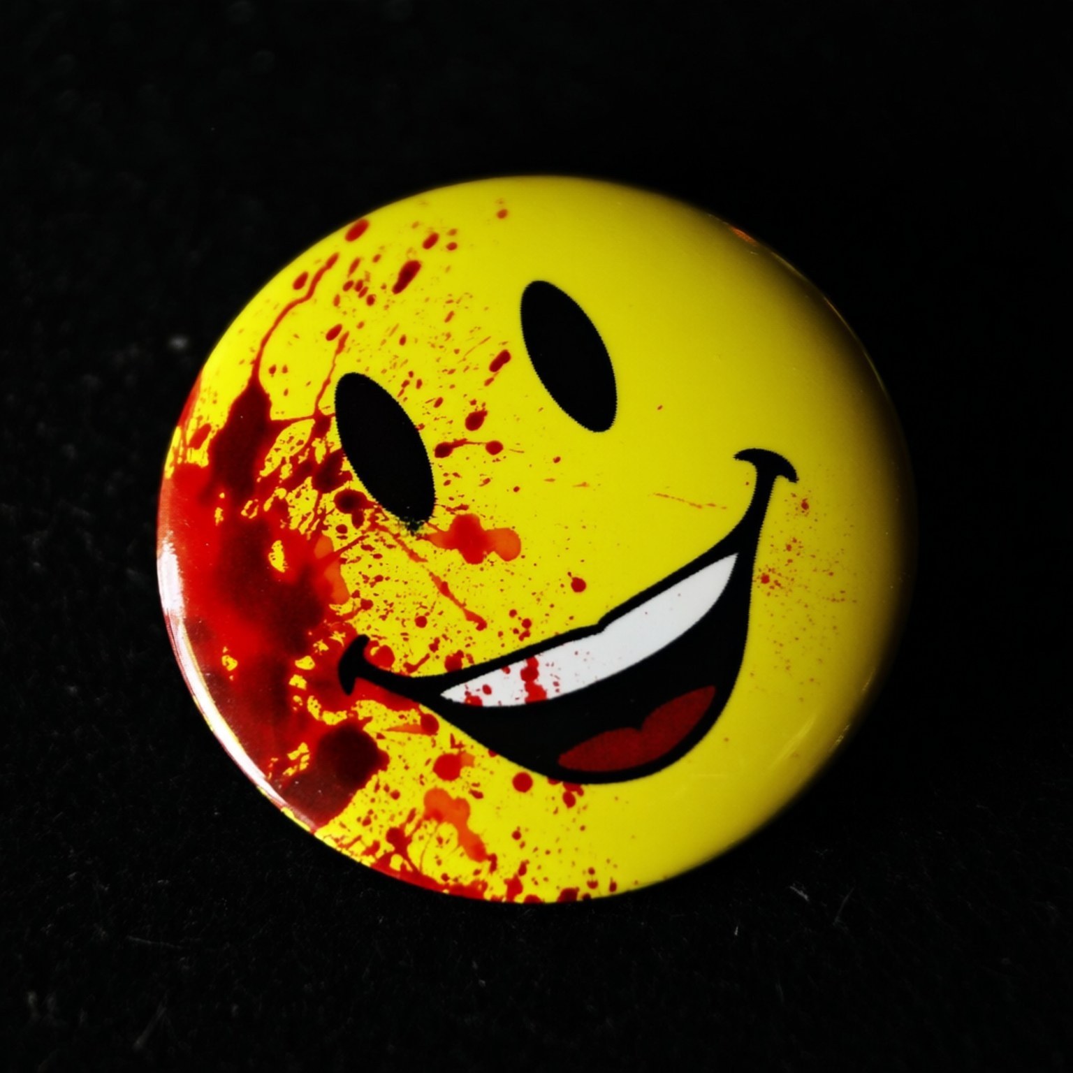 Bloody Smiley 壁紙 — 一個亮面黃色笑臉按鈕，上面濺有紅色油漆，背景為黑色。