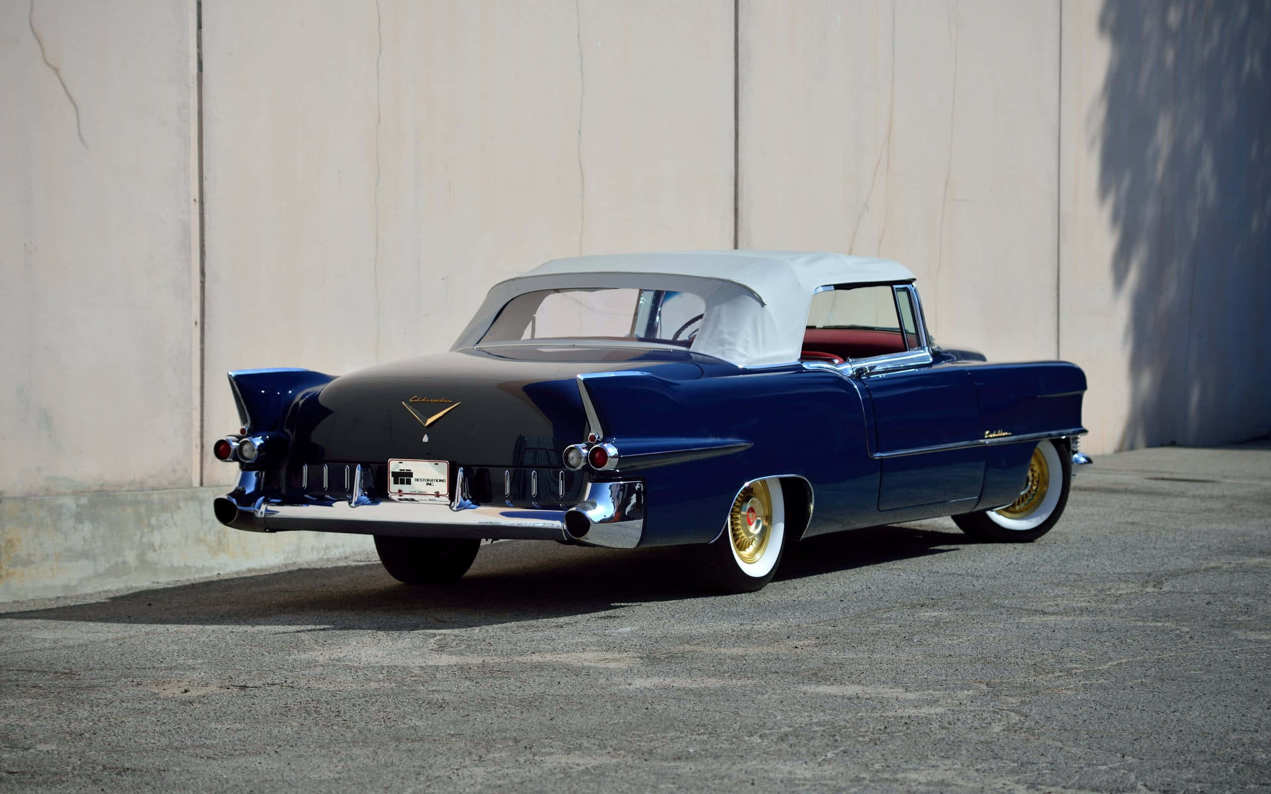 Cadillac Eldorado 桌布 壁紙 — 一輛亮面藍色經典敞篷車，白色軟頂，停在瀝青地面上的素牆旁。