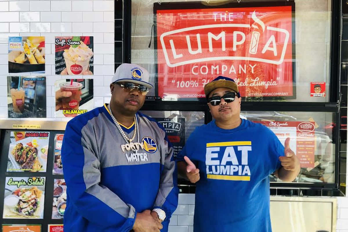  壁紙 — 兩名戴太陽眼鏡和穿隊服的男人自信地在The Lumpia Company餐車外擺姿勢，身後有菜單海報。