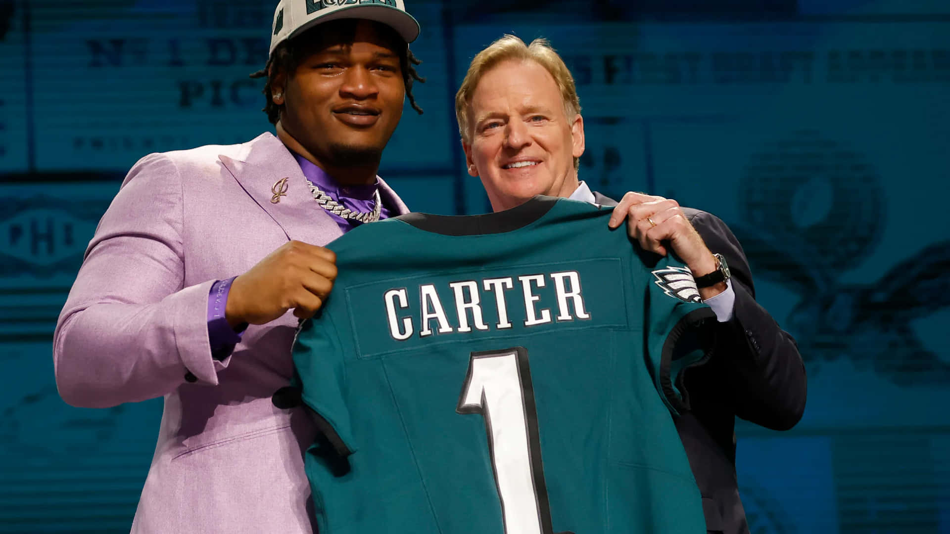  壁紙 — 兩名男子在選秀活動中微笑著舉起一件印有 'CARTER 1' 的綠色費城老鷹隊球衣。