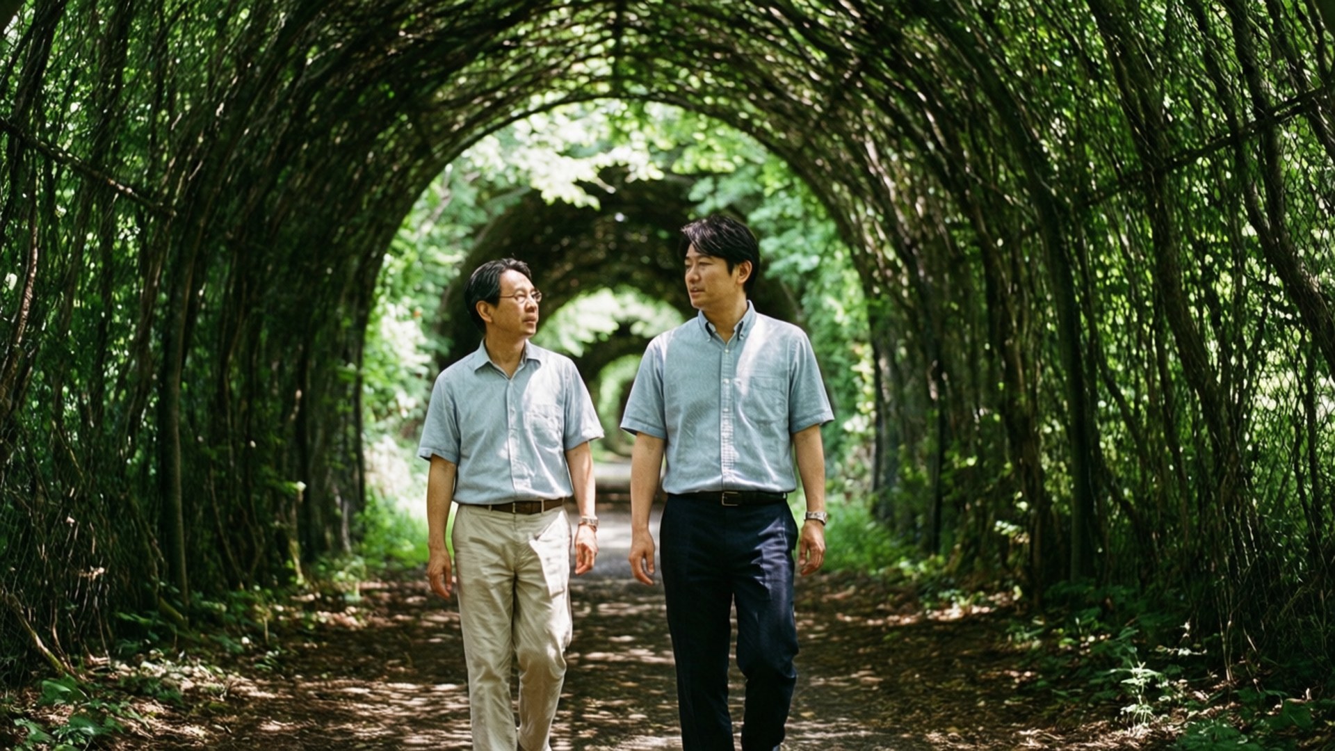 Tree Tunnel Walk 壁紙 — 兩名身穿淺色襯衫的男子在陽光斑駁的茂密綠色藤架隧道下並肩而行。
