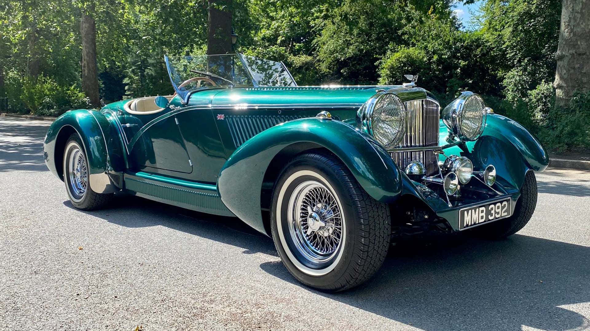Bentley Mark Vi 桌布 壁紙 — 一輛閃亮的青綠色經典敞篷跑車在明亮的陽光下閃耀，停在綠樹成蔭的柏油路上。