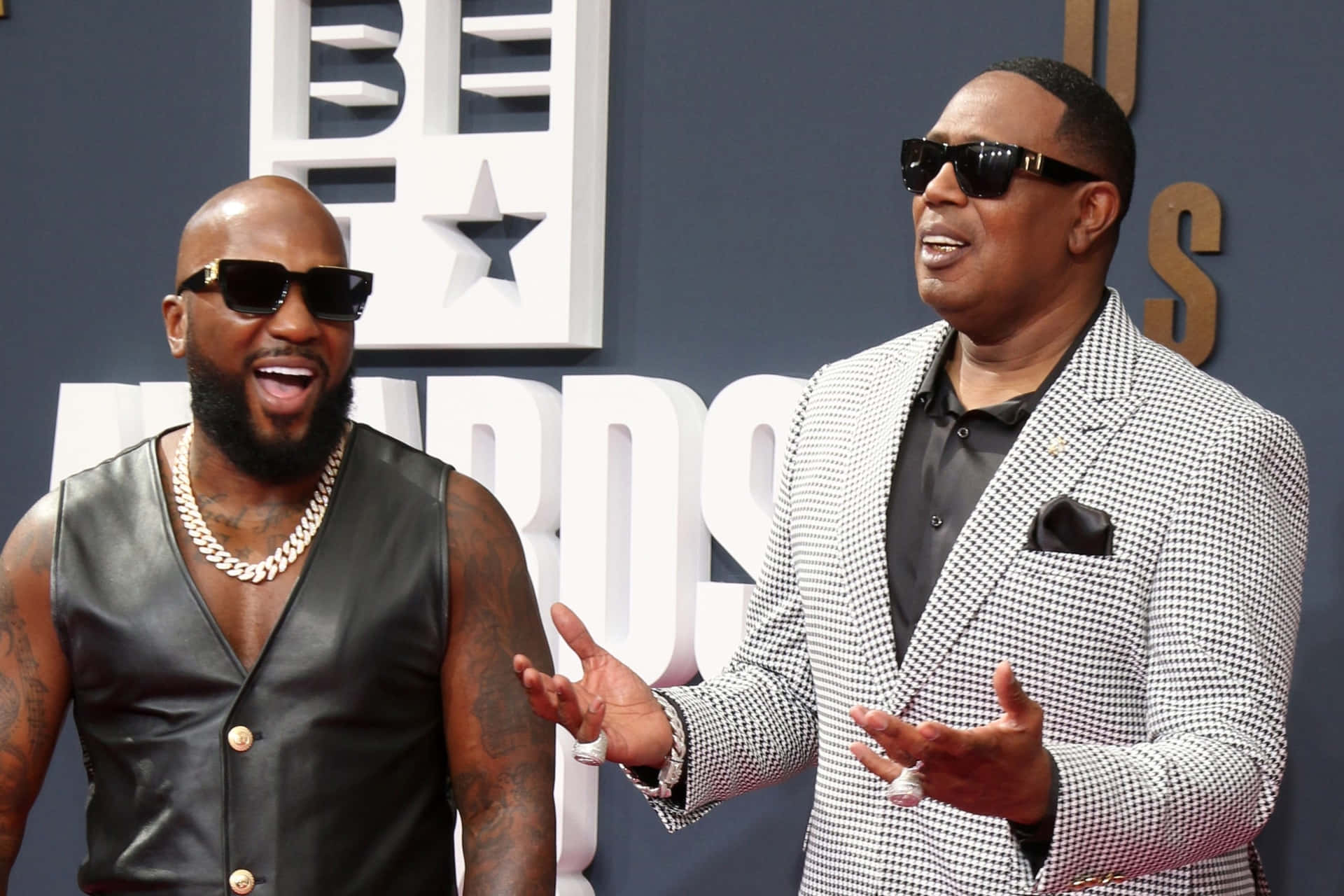 壁紙 — 兩位時尚男士戴著太陽眼鏡，在身後有「BET AWARDS」標誌的紅地毯上充滿活力地擺姿勢。