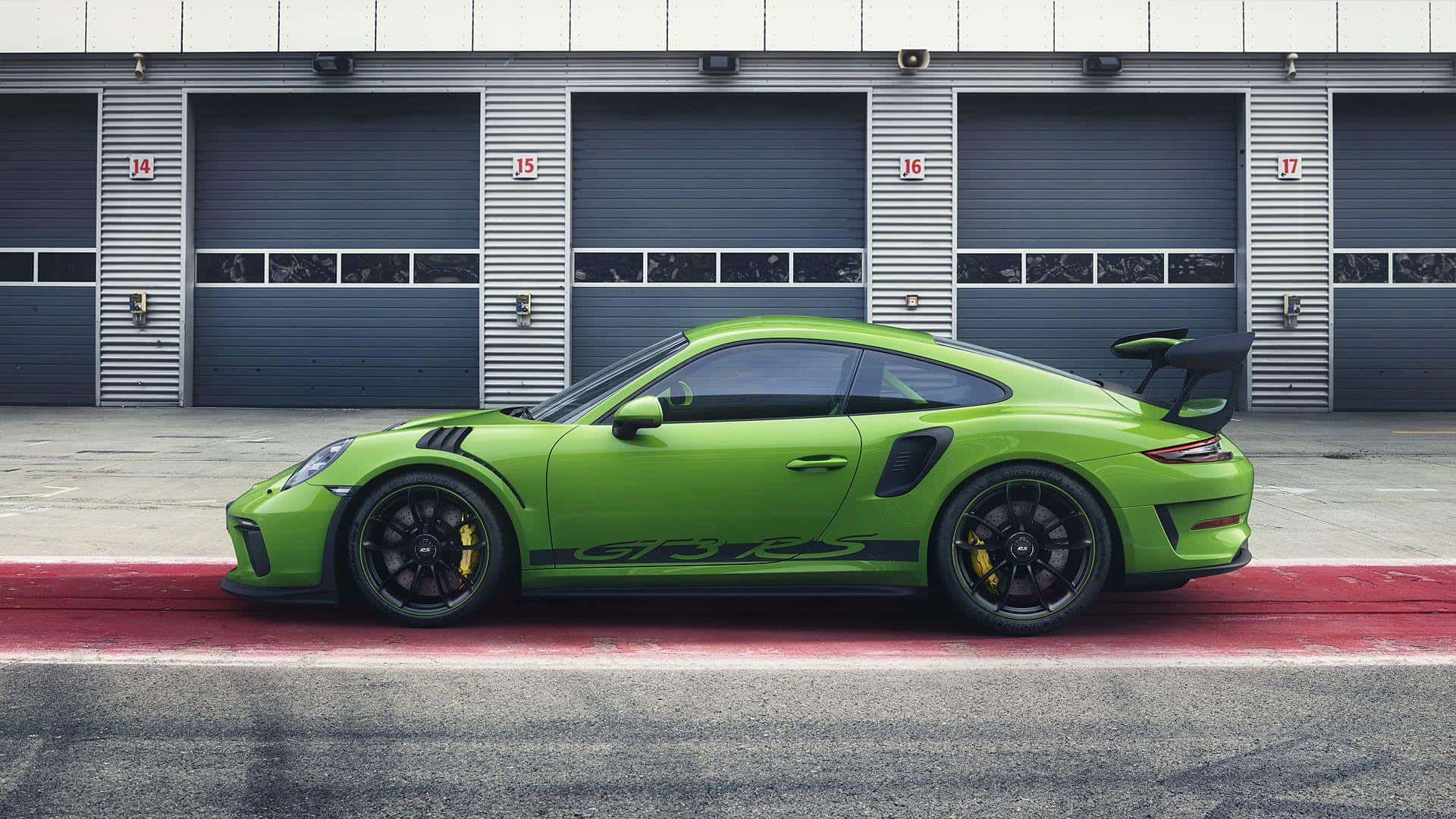  壁紙 — 一輛鮮豔的青檸綠色保時捷911 GT2 RS停放在帶有紅色路緣的工業車庫門前。