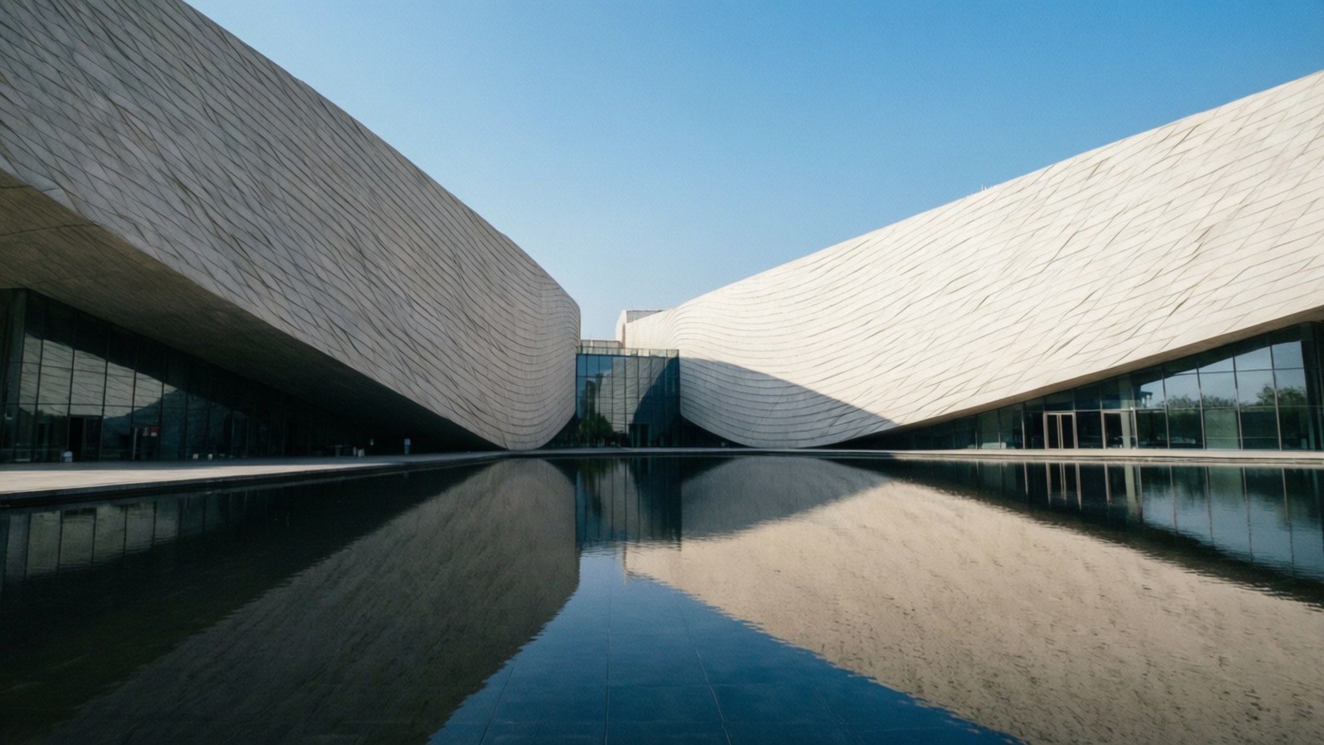 Museum Reflections 壁紙 — 兩座時尚的現代建築，帶有波紋白色外牆，在清澈的藍天下環抱著一個平靜的倒影池。