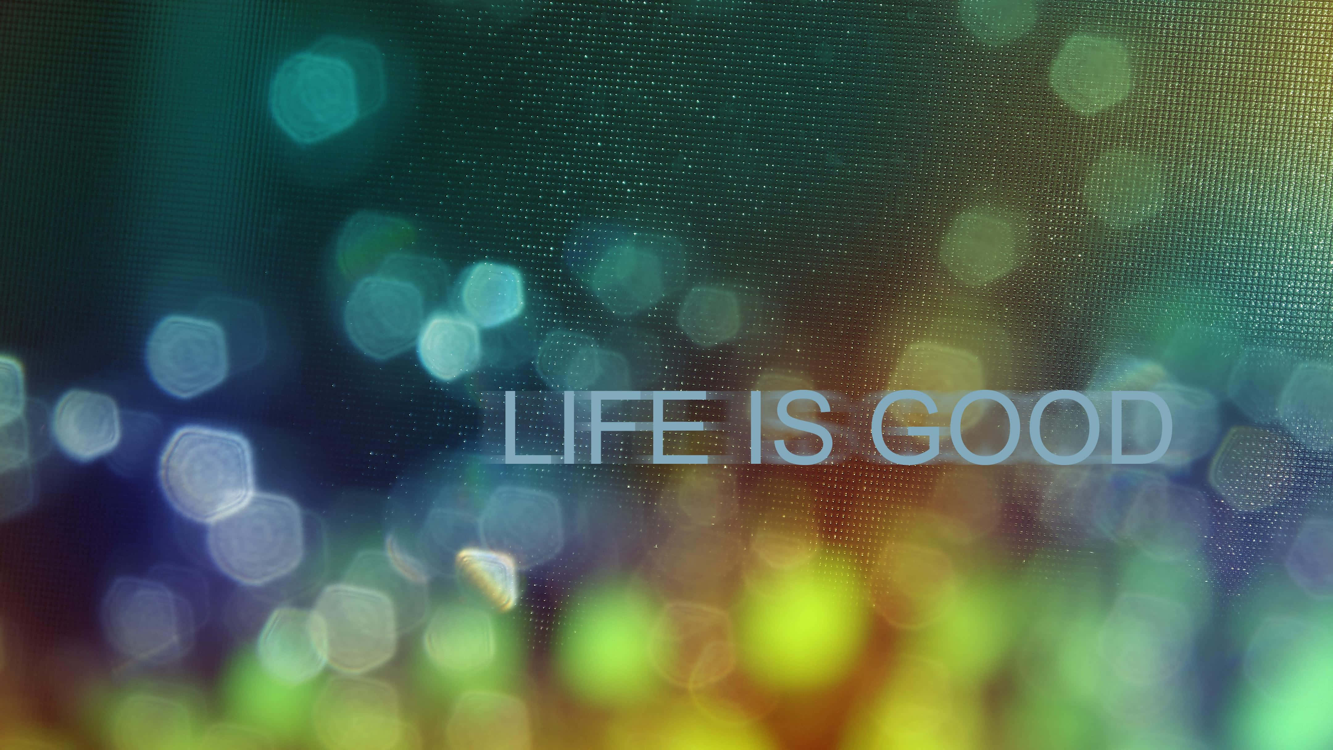 Bokeh 桌布 壁紙 — 「life is good」這個短語在充滿活力的散景背景上柔和發光，背景有青綠色、黃色和綠色的六邊形漏光。
