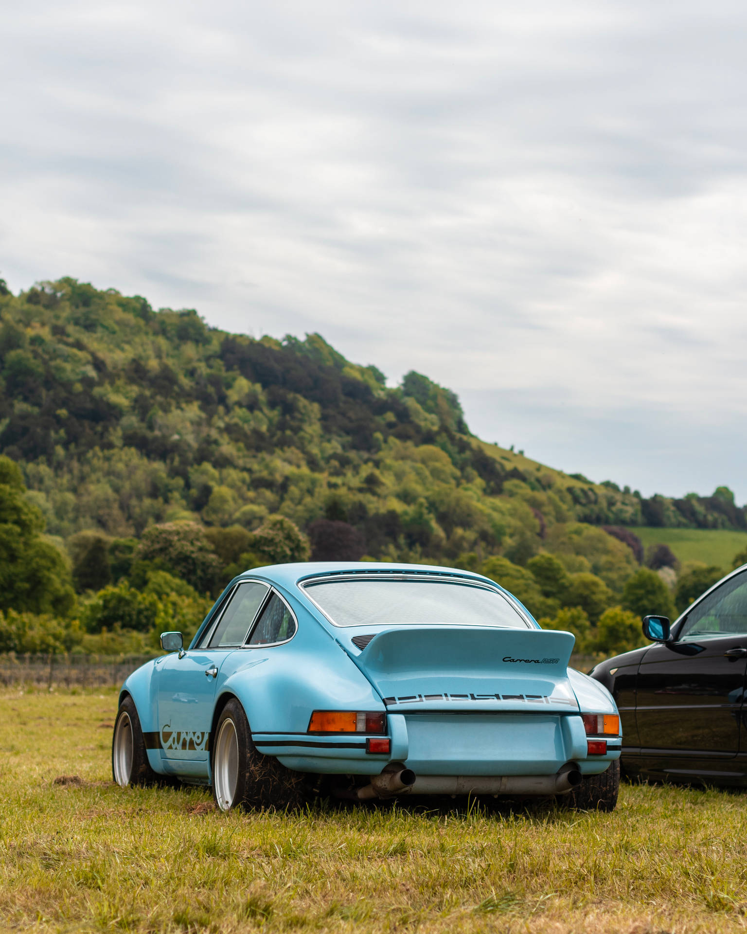 淺藍色經典保時捷911 Carrera RS停放在靠近森林山丘的草地上。 — 豪華車 壁紙