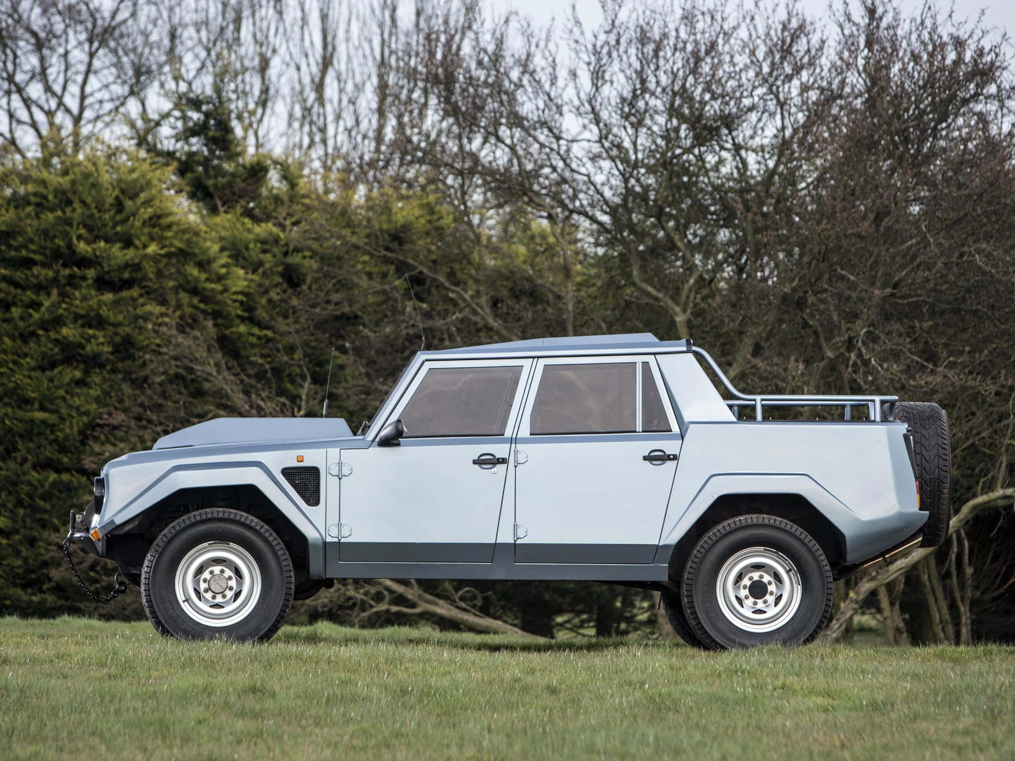 Lamborghini Lm002 桌布 壁紙 — 一輛淺藍色藍寶堅尼LM002裝甲SUV停在草地上，背景有光禿的樹木和常青樹。