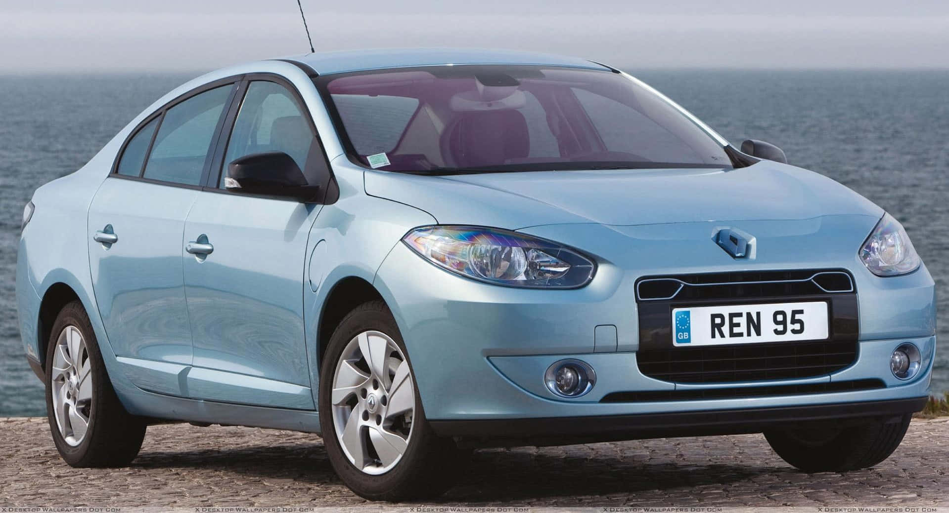 Renault Fluence 桌布 壁紙 — 一輛淺藍色雷諾轎車停泊在岩石海岸上，背景是陰天下的海浪。