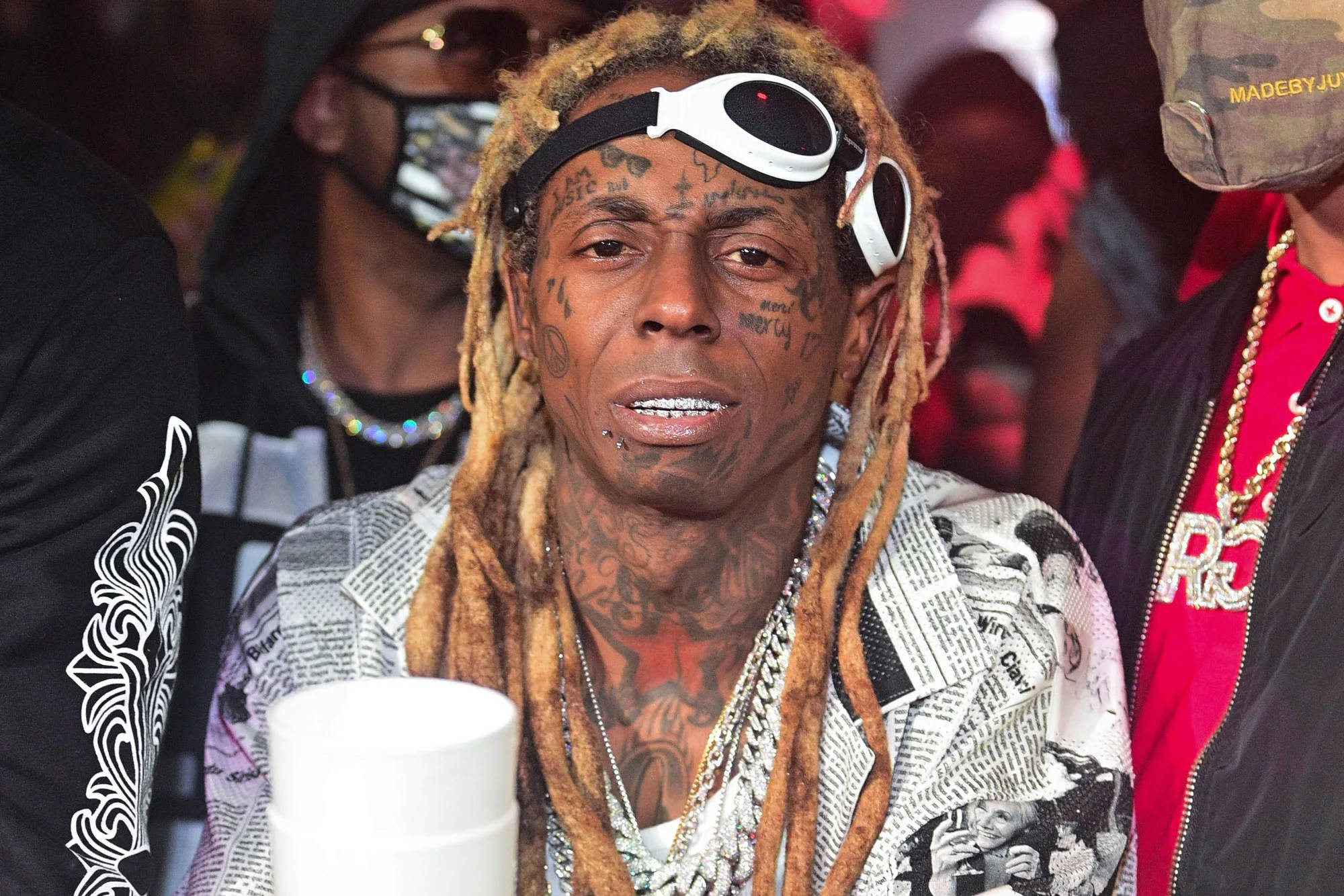 Lil Wayne 桌布 壁紙 — Lil Wayne 頭戴白色護目鏡，身穿報紙印花外套，在活動中被人群包圍。