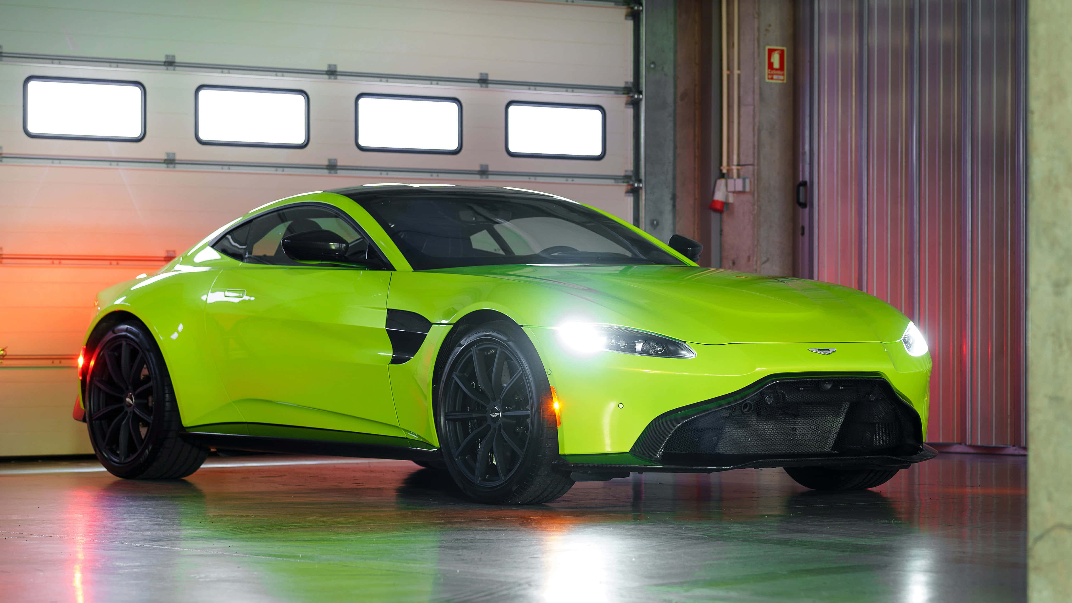 Aston Martin Vantage 桌布 壁紙 — 一輛充滿活力的萊姆綠色 Aston Martin Vantage 在車庫燈光下閃耀，帶有黑色飾邊和發光的車頭燈。