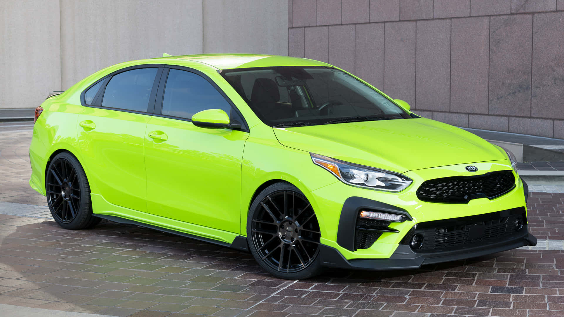 Kia Forte 桌布 壁紙 — 一輛充滿活力的萊姆綠色Kia轎車，搭配黑色輪圈，停在石牆旁的磚砌路面上。
