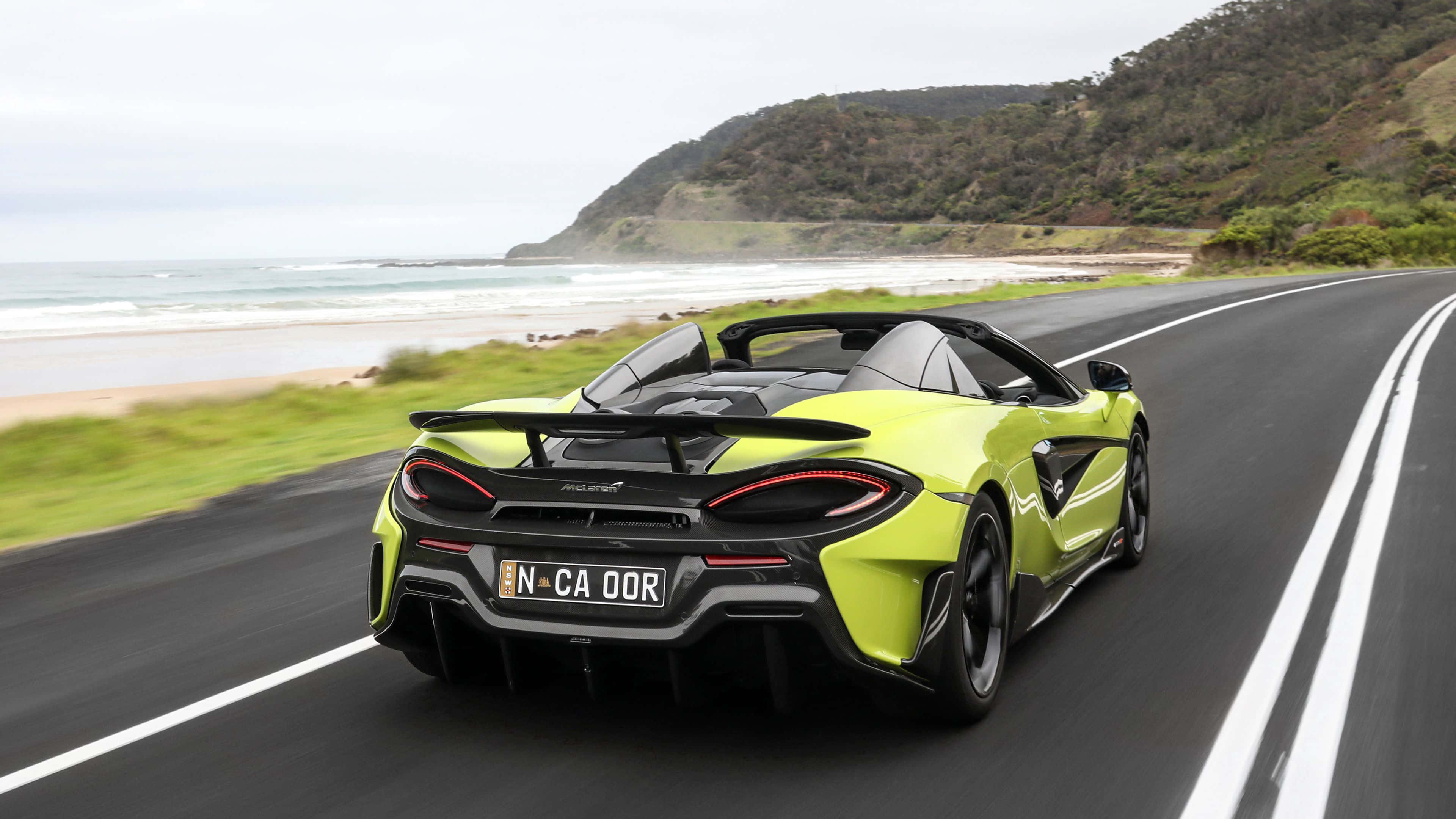 Mclaren 600lt 桌布 壁紙 — 一輛萊姆綠色的McLaren跑車沿著海岸公路疾馳，背景中海浪拍打懸崖。