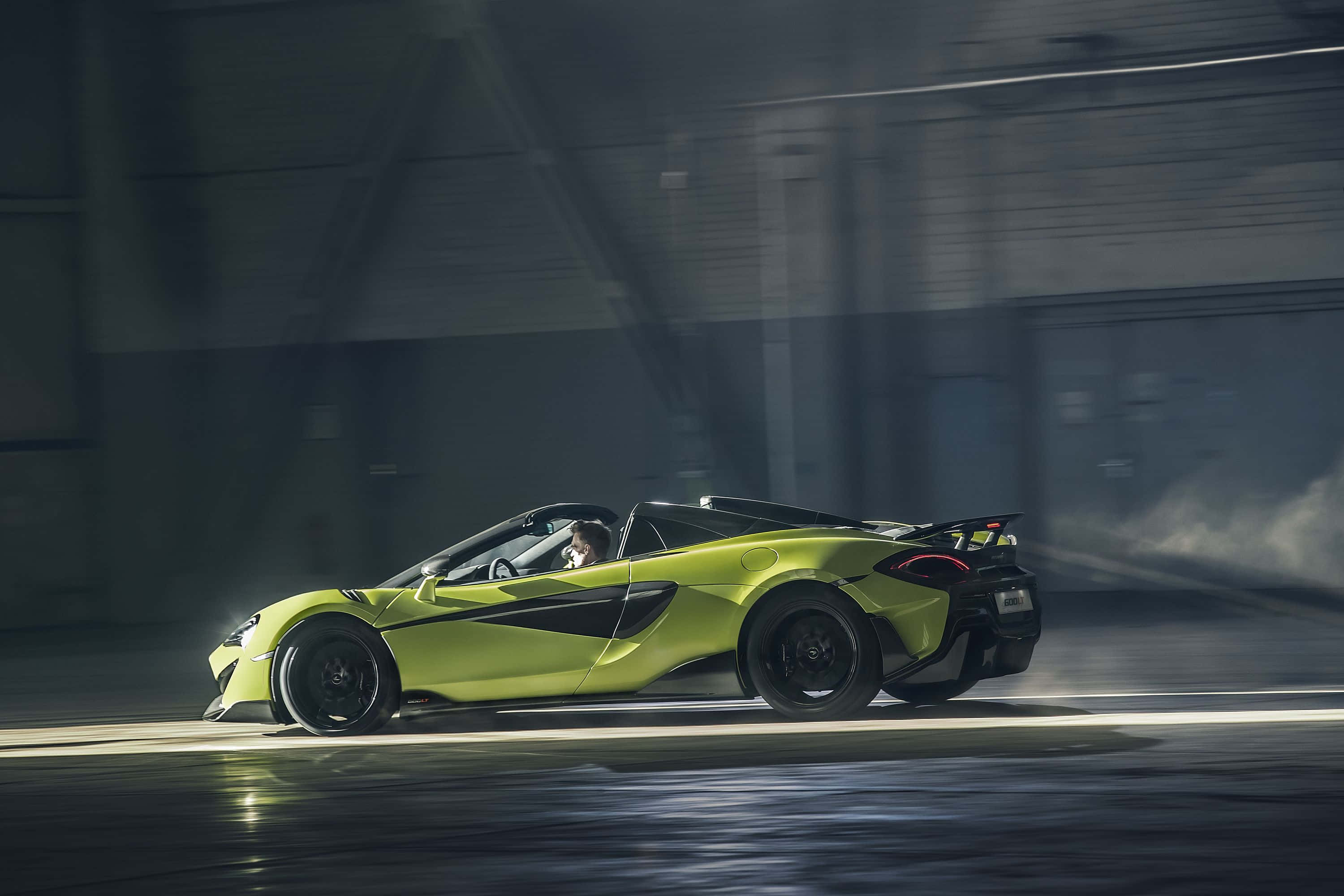 Mclaren 600lt 桌布 壁紙 — 一輛萊姆綠色的McLaren跑車在昏暗的工業車庫中疾馳，帶有動態模糊和戲劇性燈光。