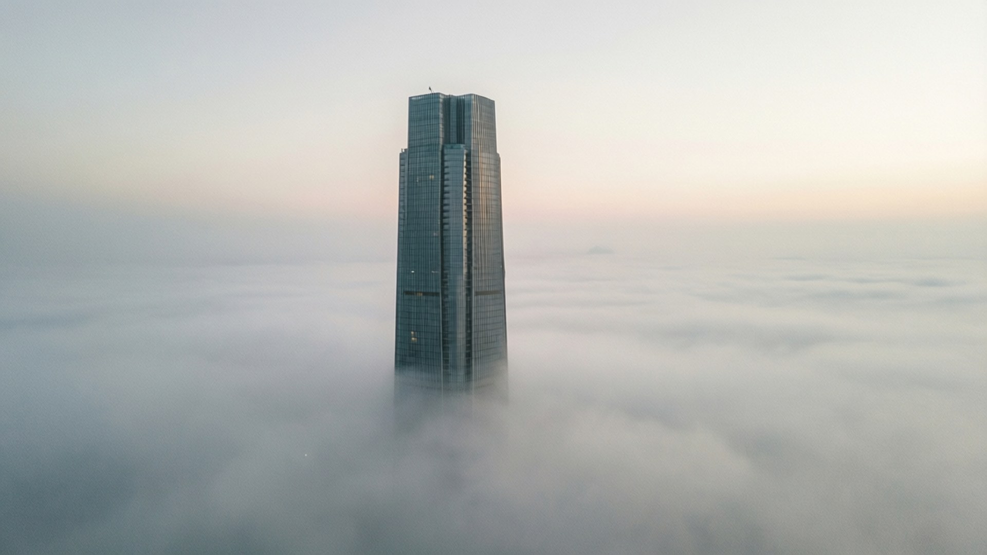 Mist at Dawn 壁紙 — 黎明時分，一座高聳的玻璃摩天大樓穿透厚厚的霧靄，上方是柔和的粉紅色和灰色天空。