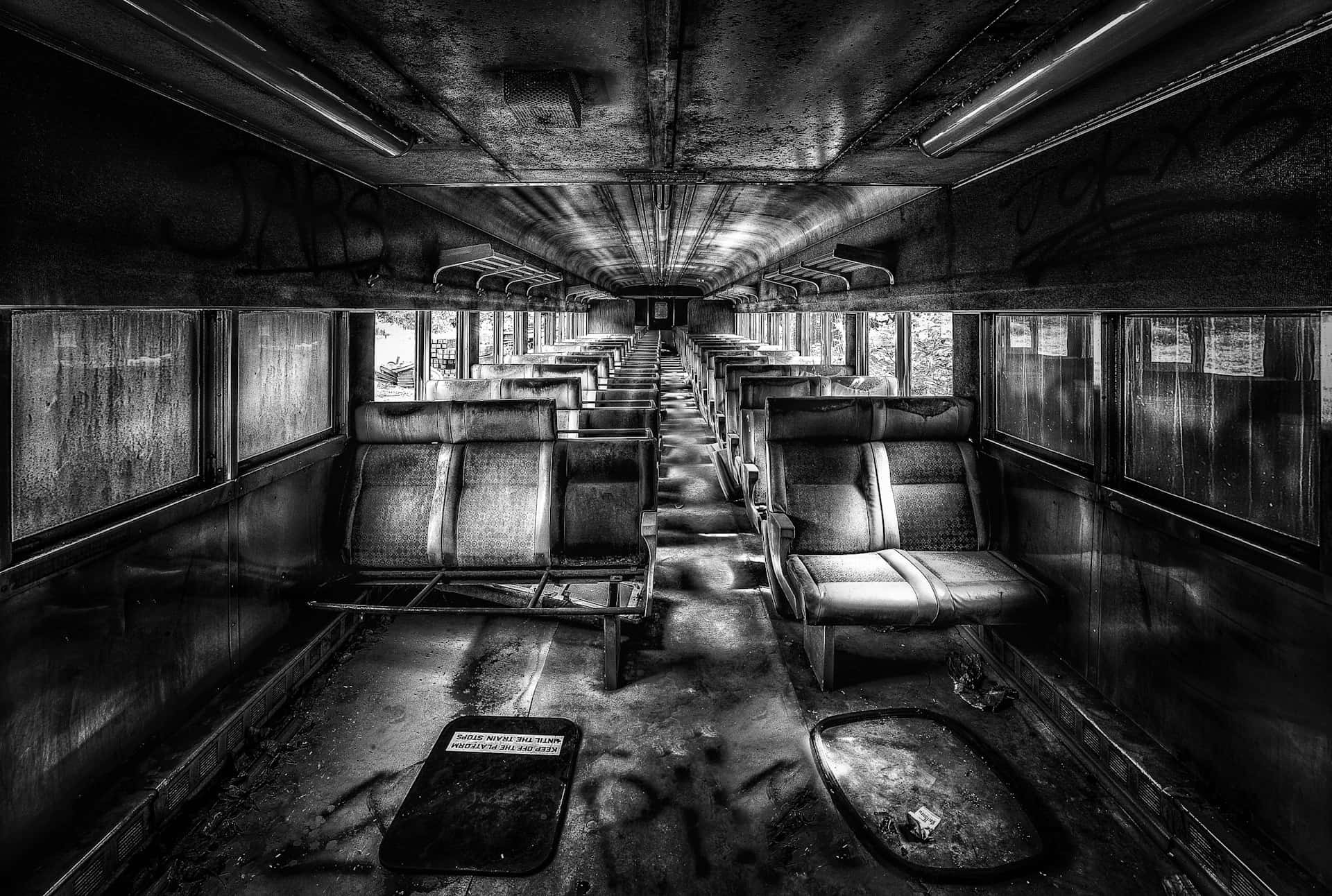  壁紙 — 一個令人毛骨悚然的黑白視角，俯瞰廢棄火車車廂內空蕩蕩、腐朽的走廊，牆上有塗鴉，座位破損。