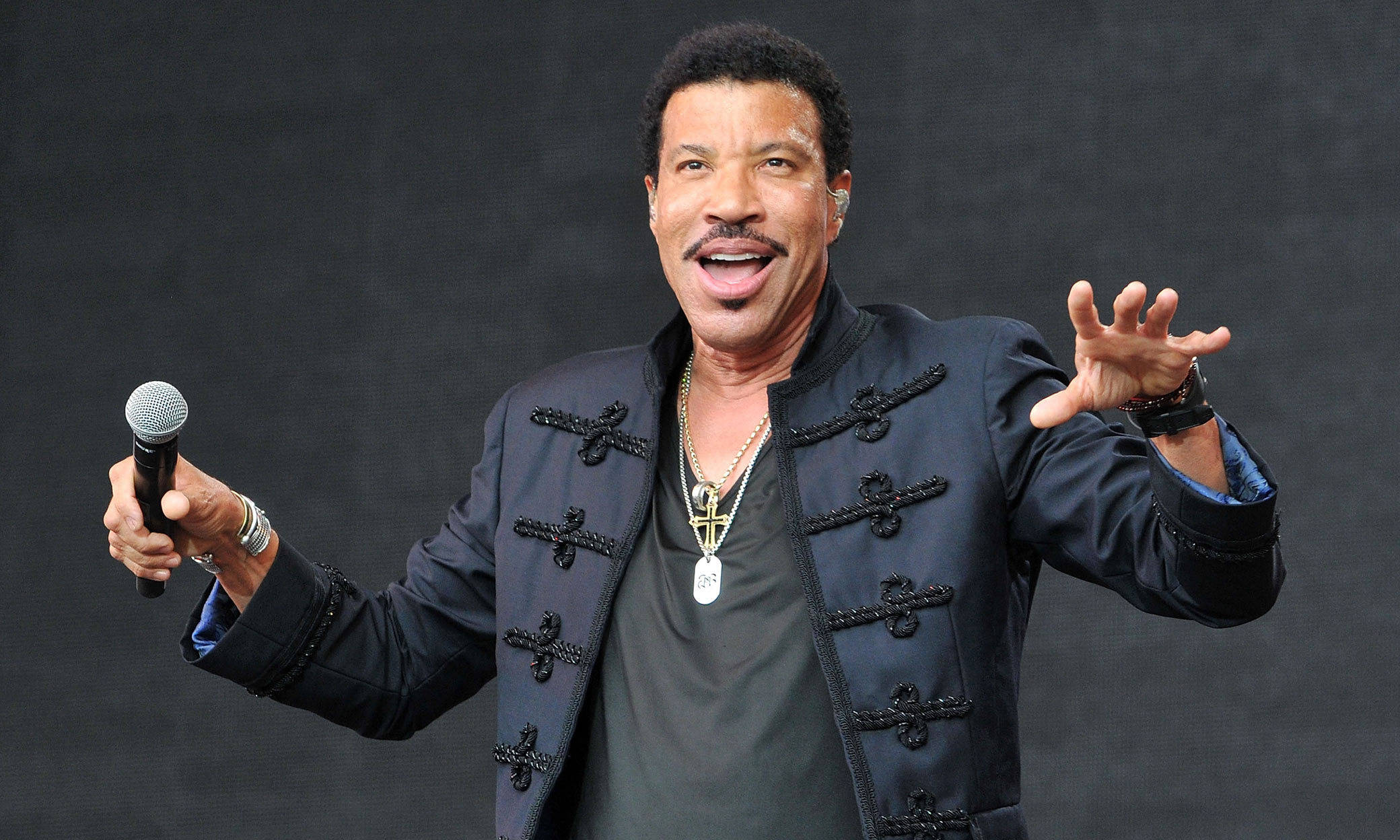 Singing 桌布 壁紙 — Lionel Richie 手持麥克風，在深色紋理背景前充滿活力地表演。