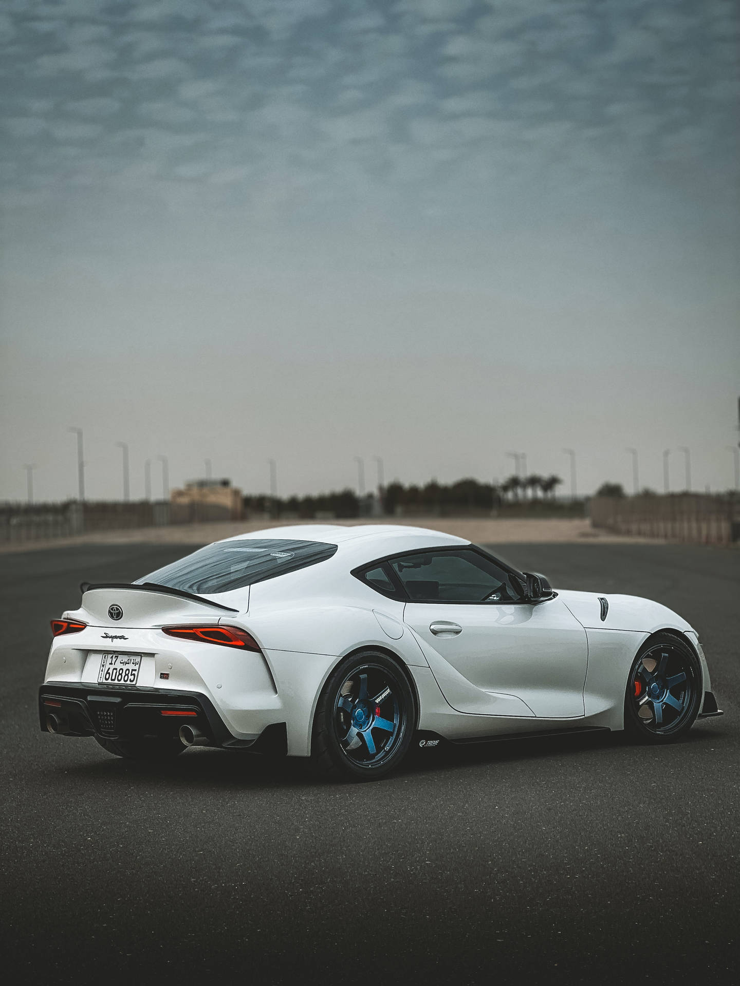 陰天天空下，空曠賽道上的白色豐田Supra，帶藍色制動卡鉗。 — Toyota Supra 壁紙