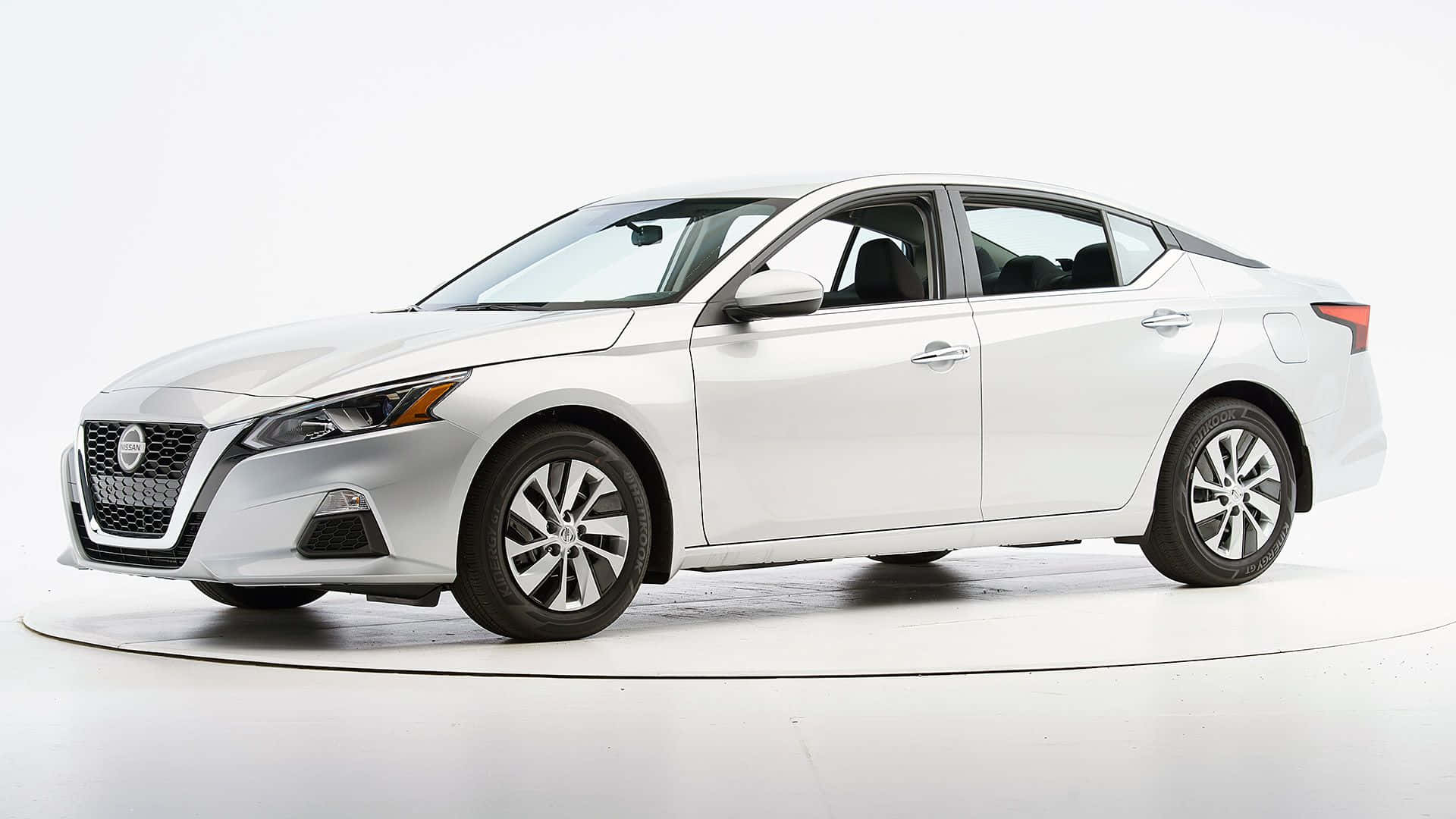 Nissan Altima 桌布 壁紙 — 一輛流線型白色日產轎車在乾淨的攝影棚中展示，配有柔和燈光和簡約白色地板。