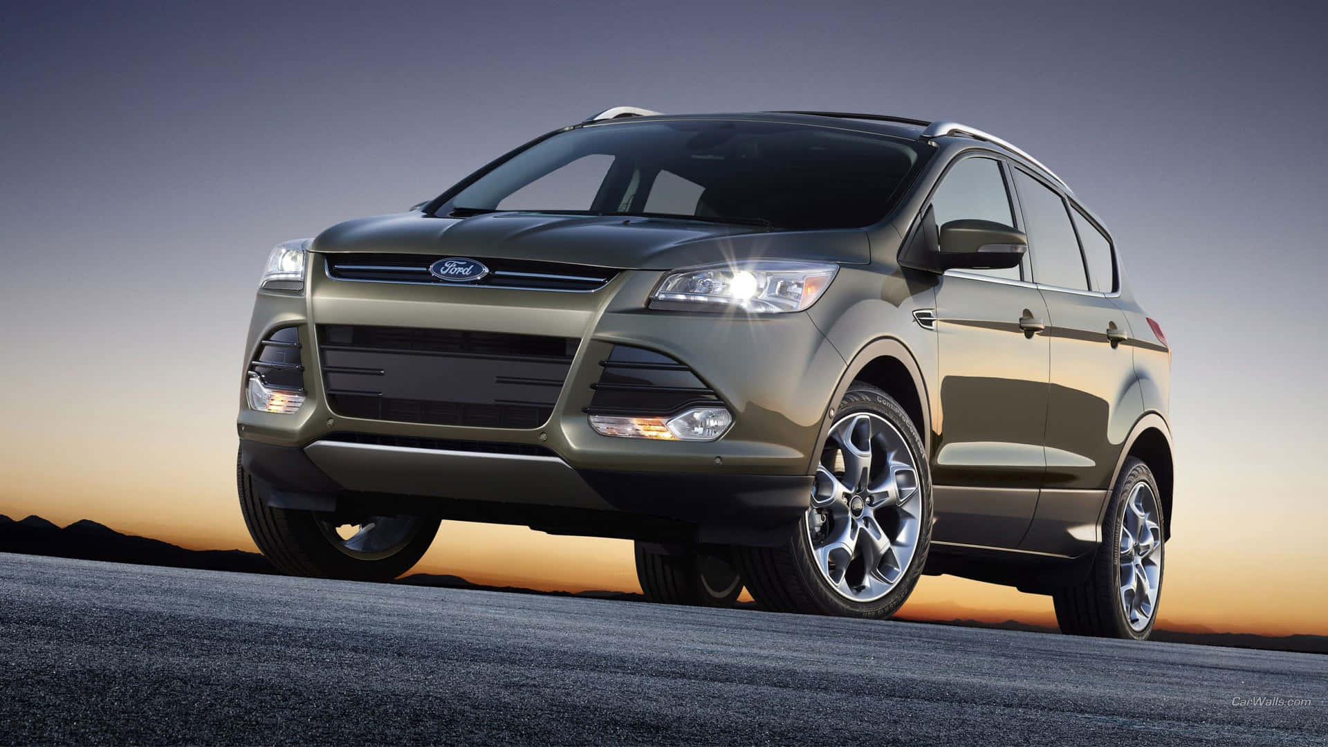 Ford Escape 桌布 壁紙 — 一台流線型橄欖綠色福特Escape SUV在夕陽下閃耀，行駛在沙漠公路上，遠方有山脈。