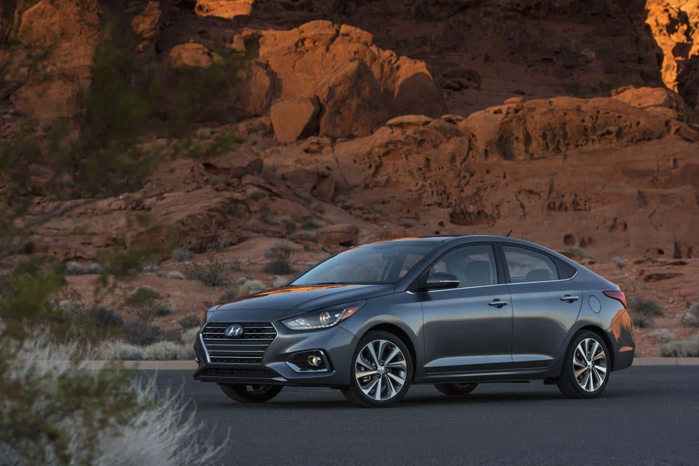 Hyundai Accent 桌布 壁紙 — 一輛流線型灰色轎車停在沙漠公路上，紅色岩層在溫暖的日落光芒中閃耀。