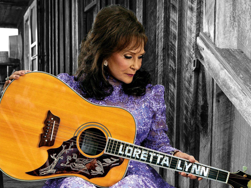 Loretta Lynn 在木質背景前手持吉他。 — 吉他動圖 壁紙