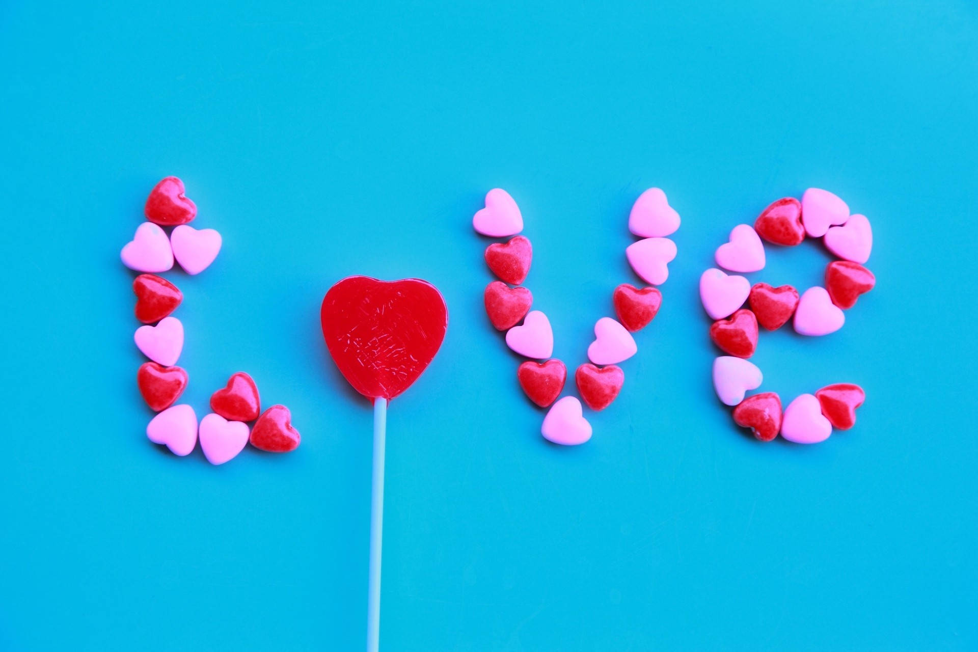 愛心 桌布 壁紙 — 「love」這個字由心形糖果和紅色心形棒棒糖在明亮藍色背景上拼出。